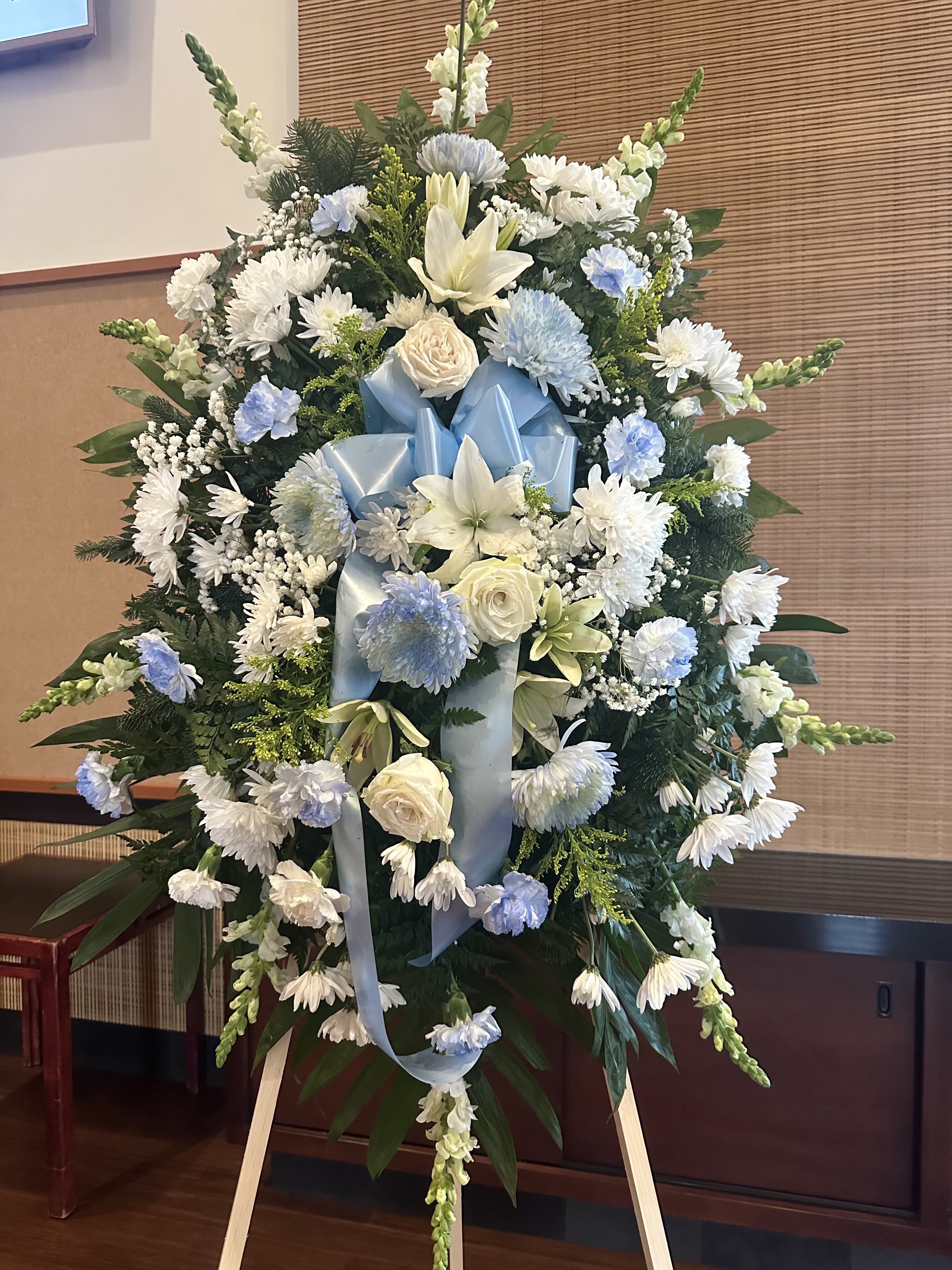 Large white and pale blue funeral spray on an easel