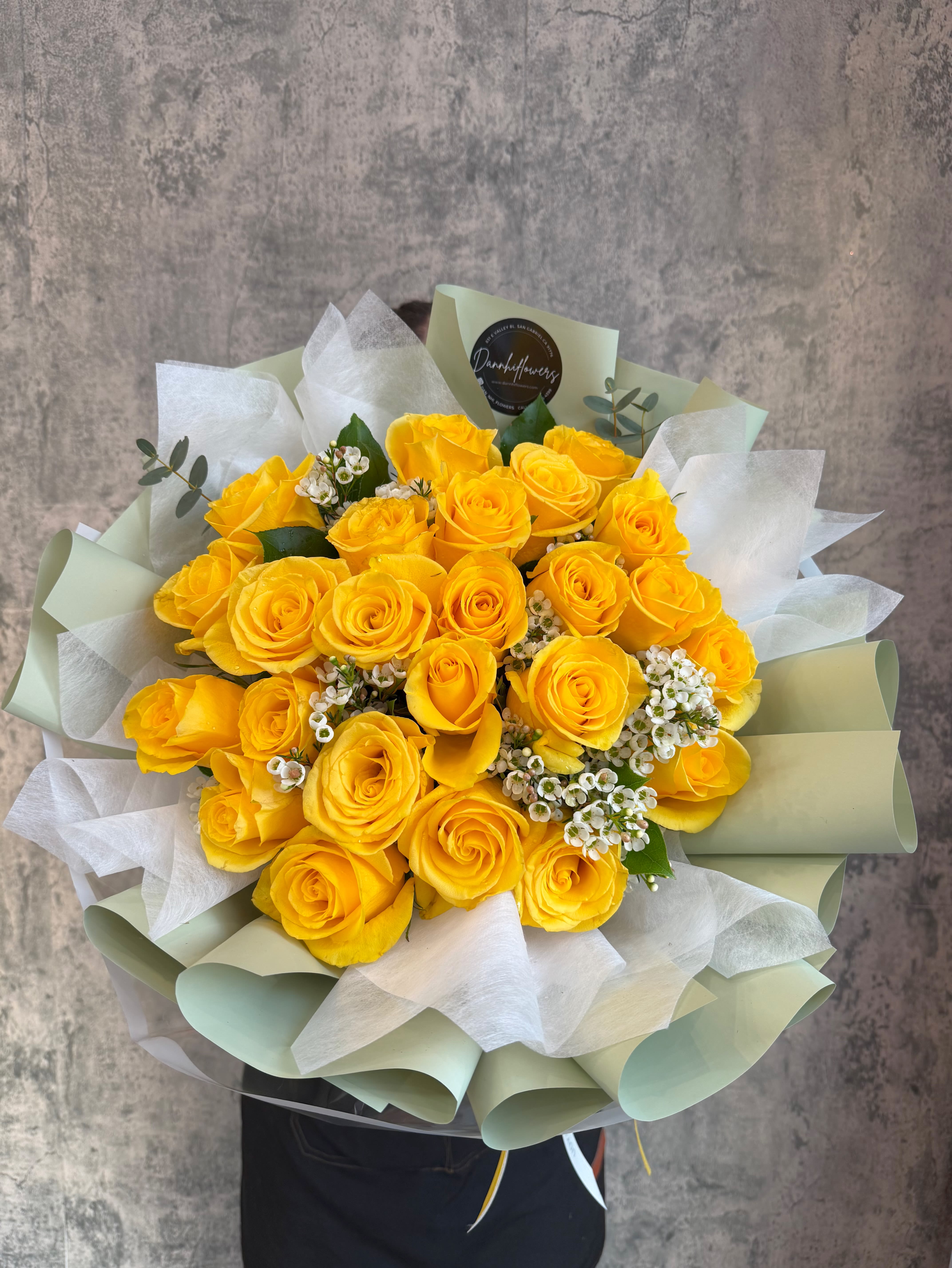 Bouquet of yellow roses with white filler flowers wrapped in pale paper