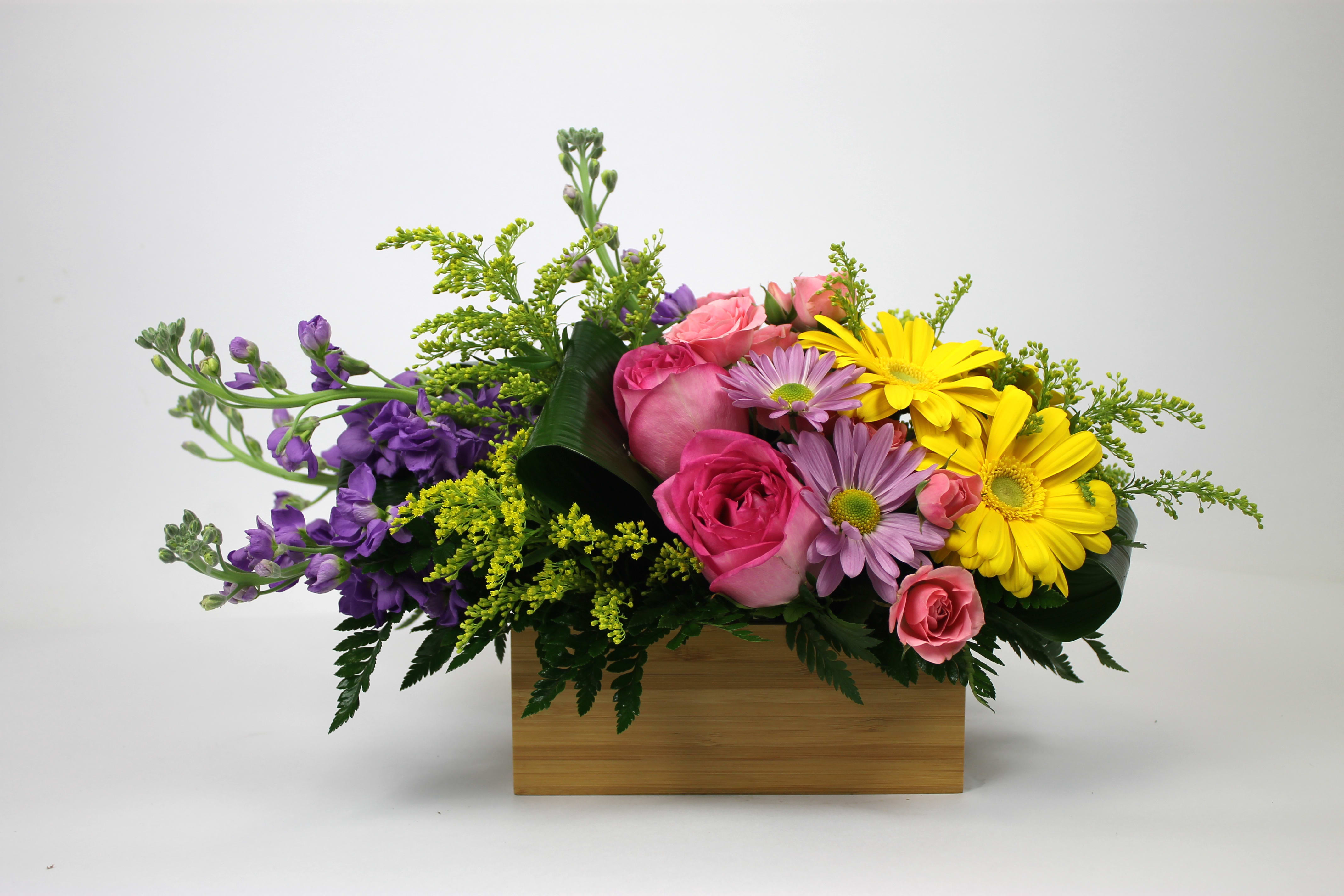 Mixed bouquet of pink roses, yellow daisies, and purple flowers in a wooden box