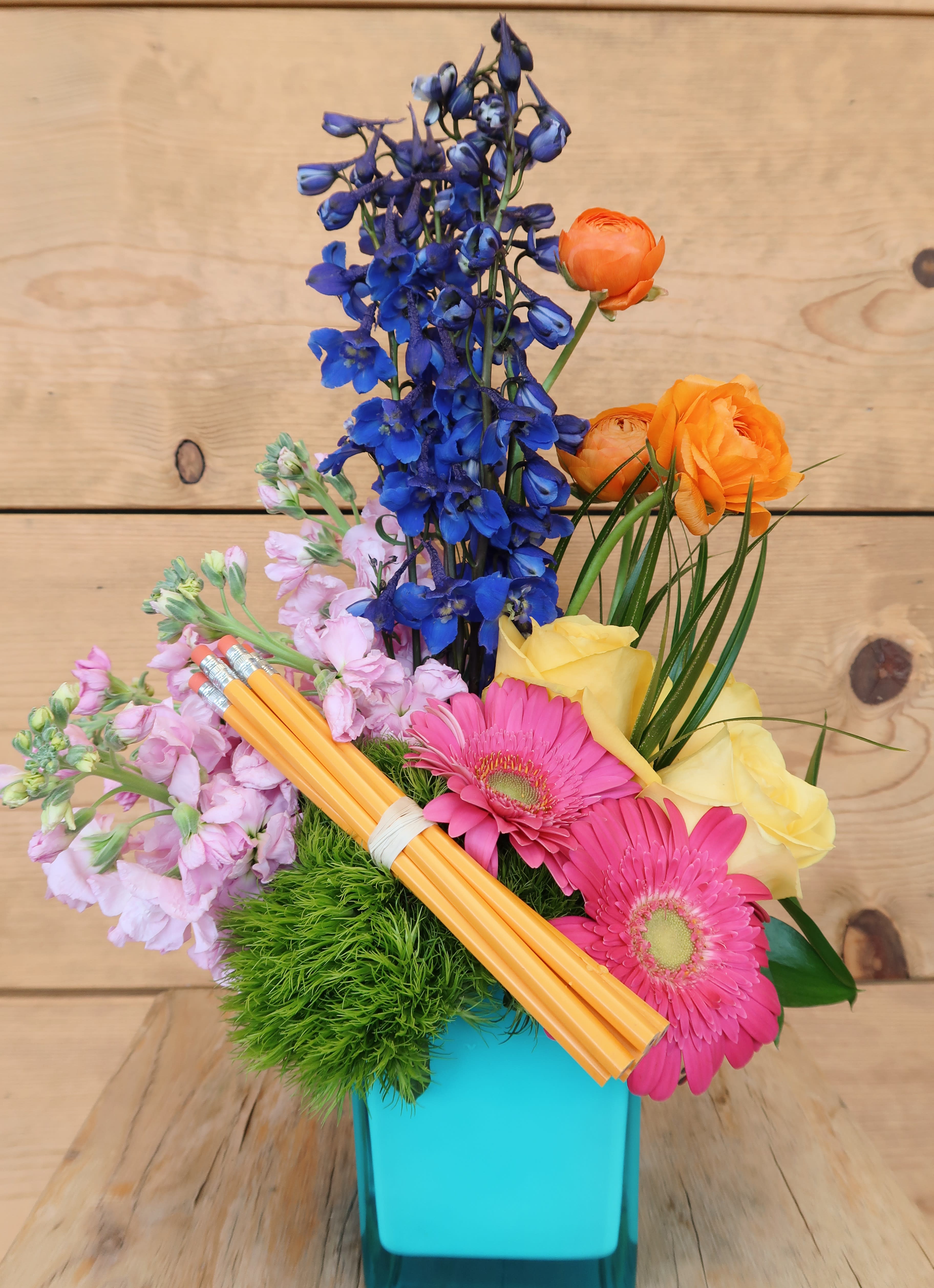 Colorful bouquet in a turquoise vase with blue, pink, yellow, and orange flowers
