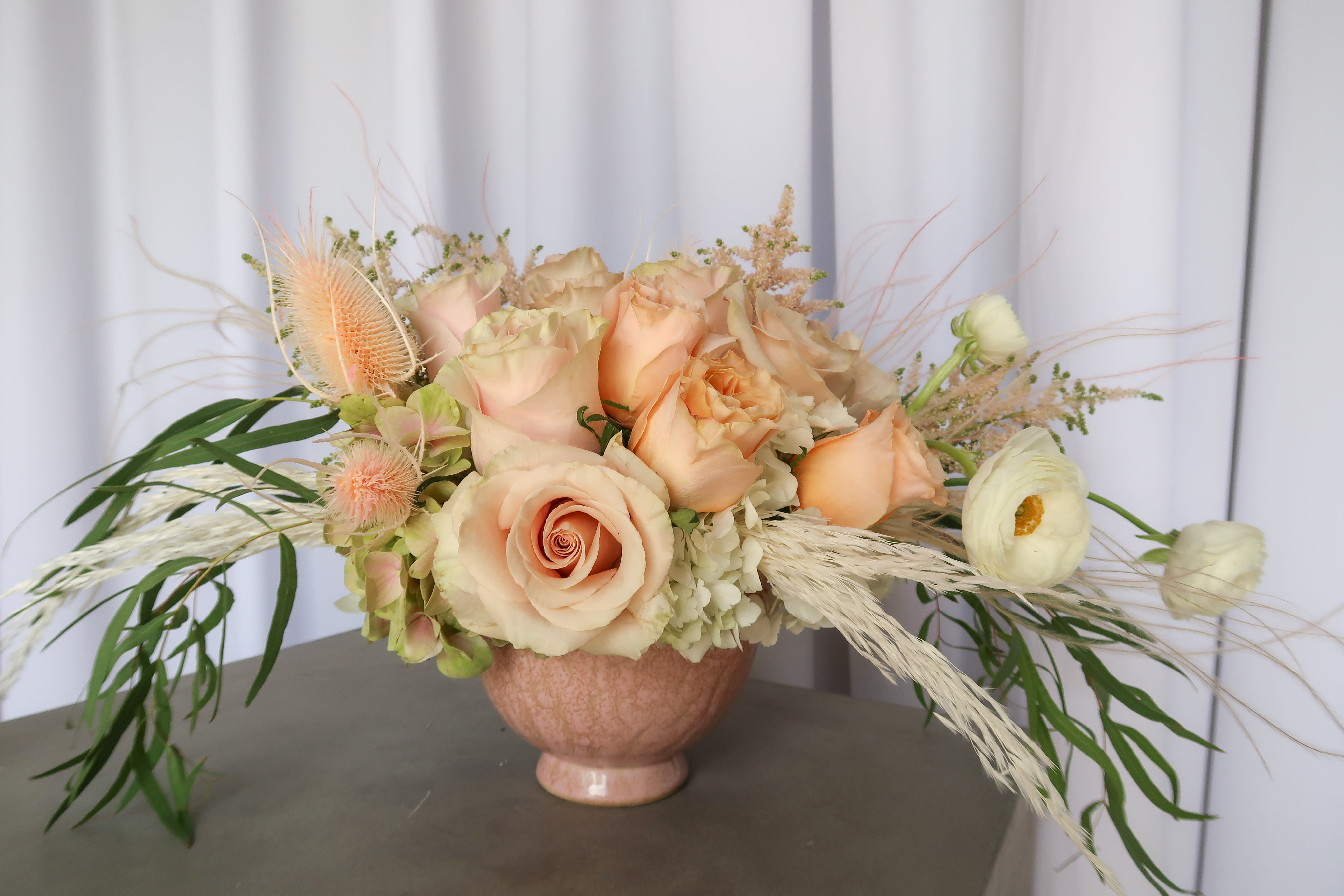 Peach roses and white ranunculus in a pink vase