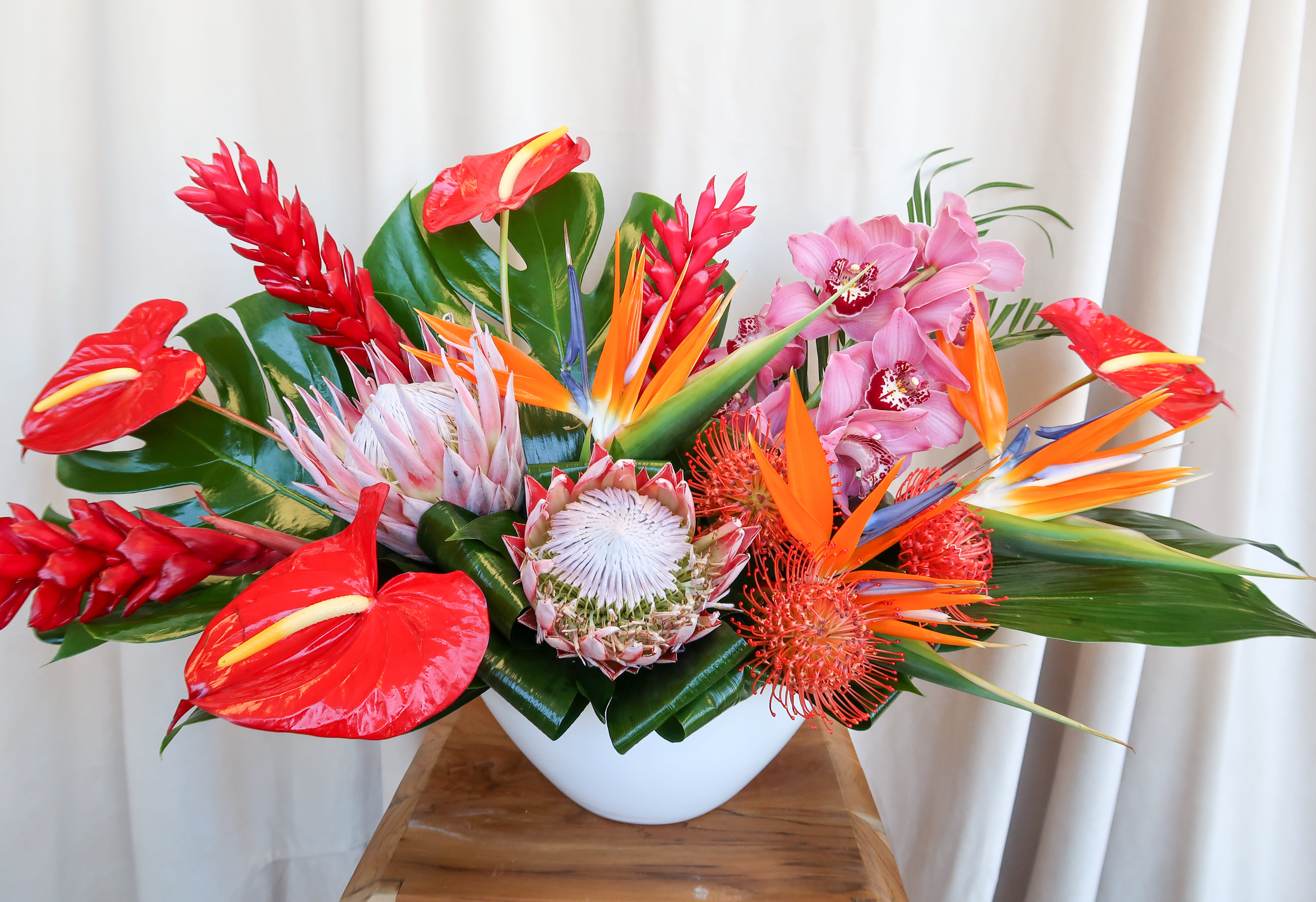Tropical flower arrangement in a white bowl vase with red, orange, pink, and white blooms