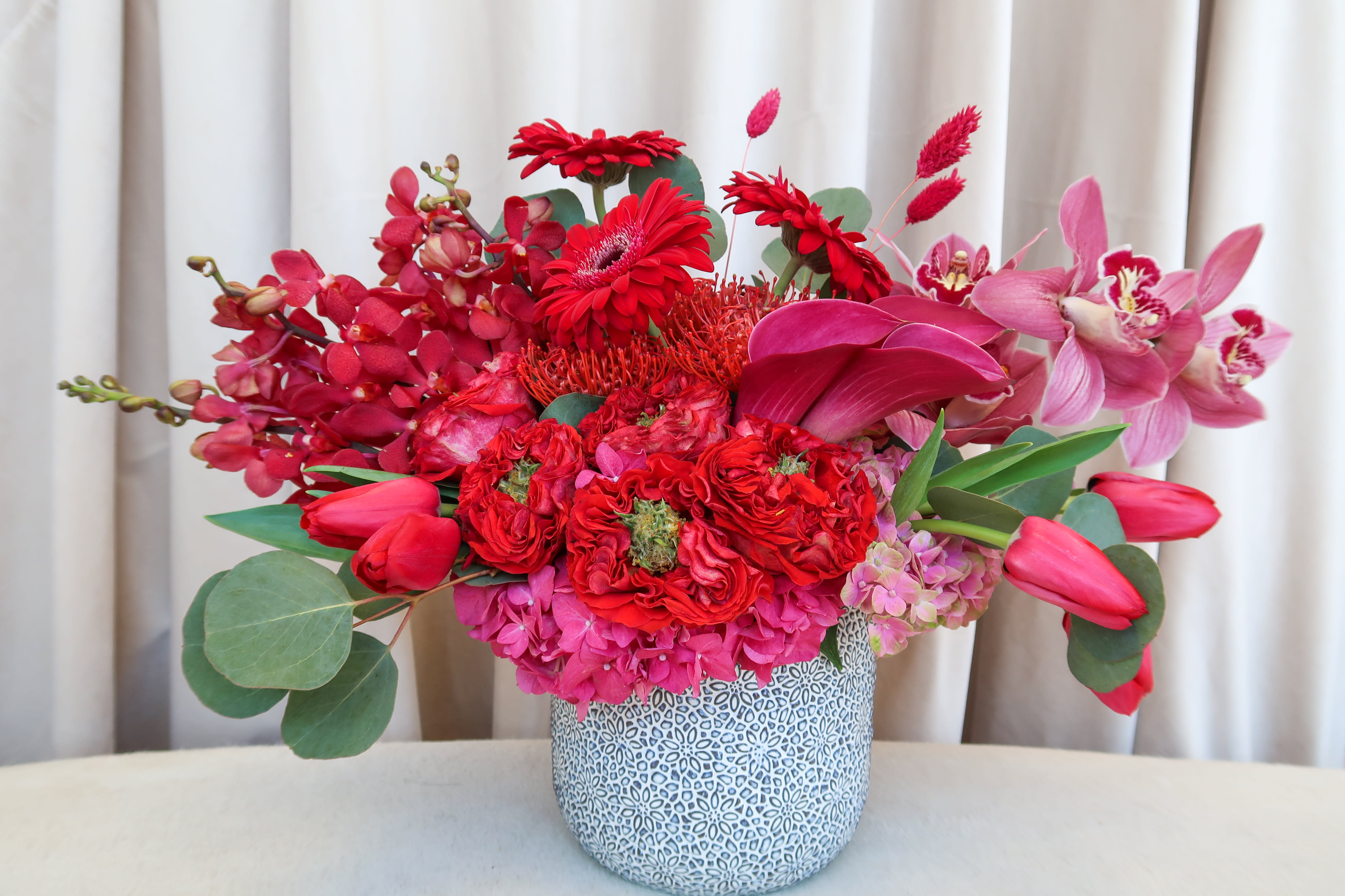 Red and pink floral arrangement in a patterned ceramic vase