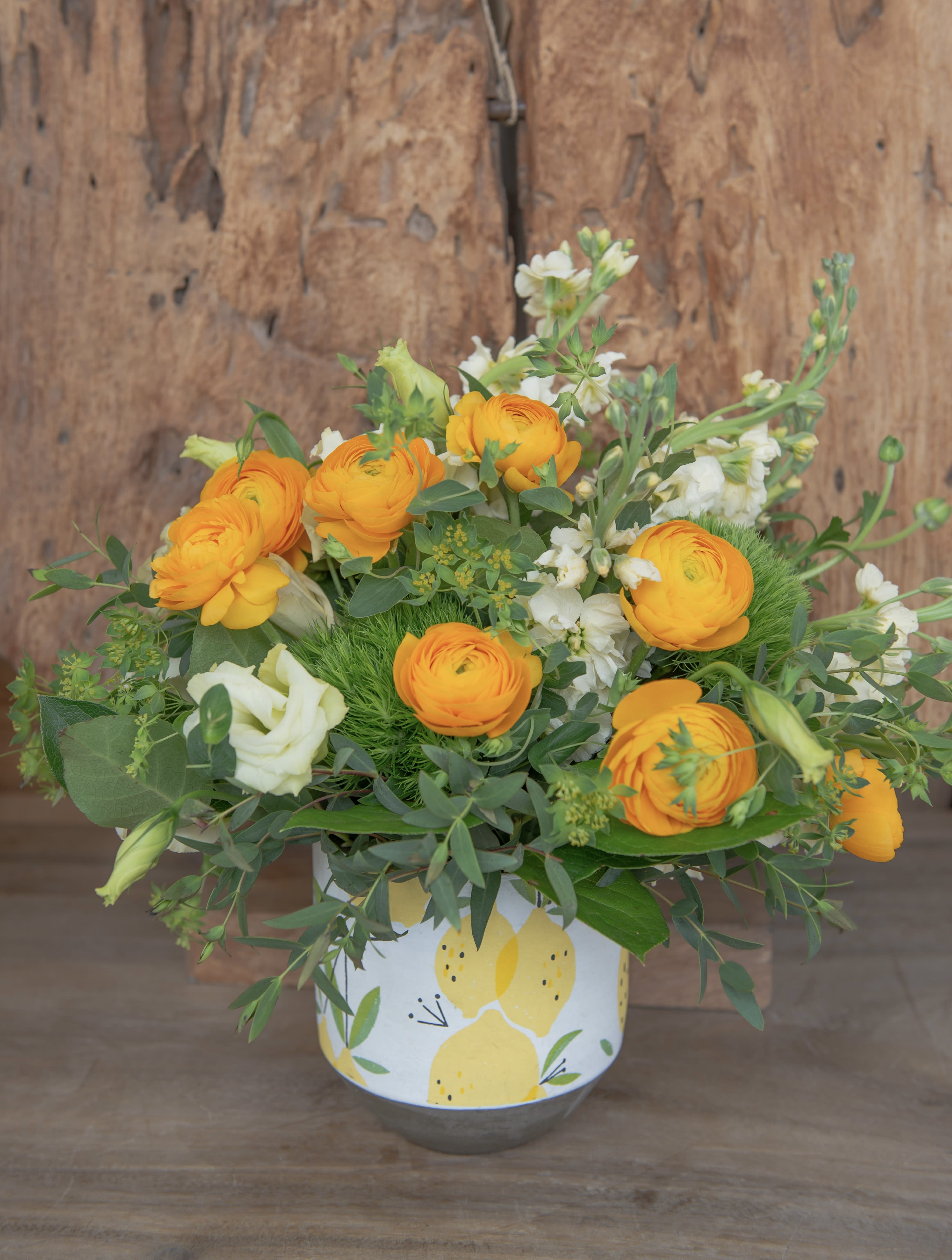 Orange ranunculus and white blooms in a lemon-patterned container