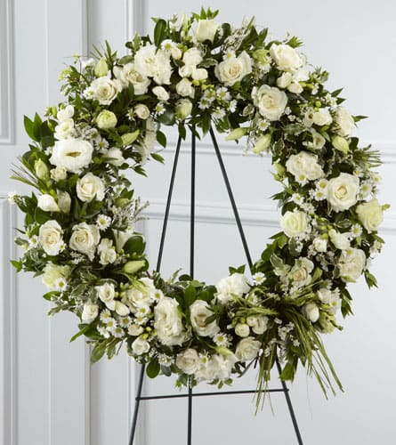 White floral wreath on a black stand with roses and small daisies