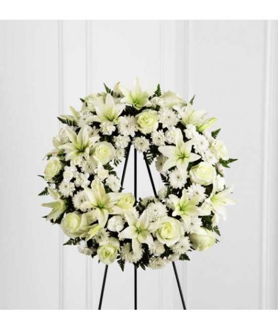 White floral wreath on a black stand with lilies and roses