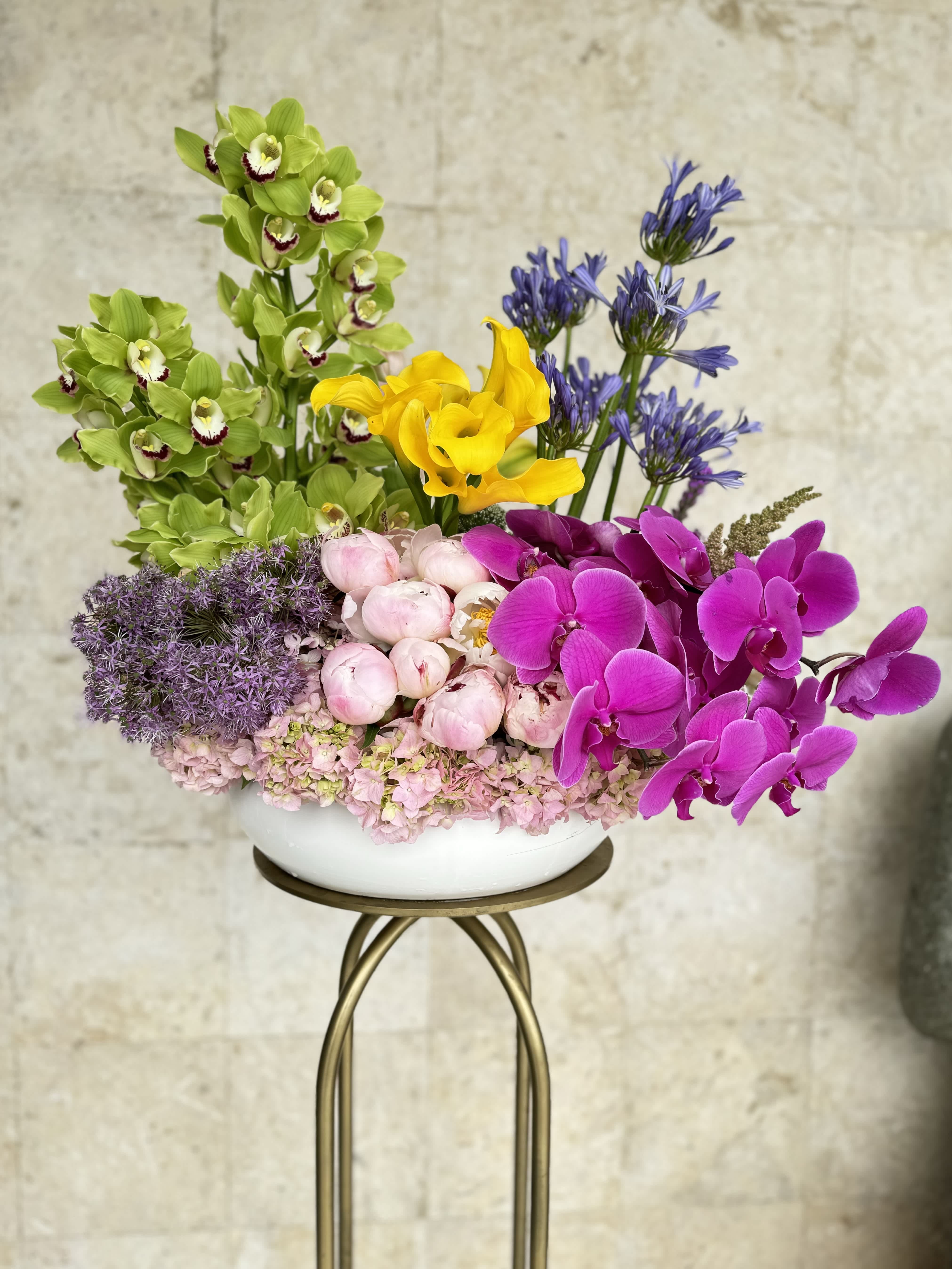 Colorful floral arrangement with orchids, calla lilies, peonies, and hydrangeas in a white bowl