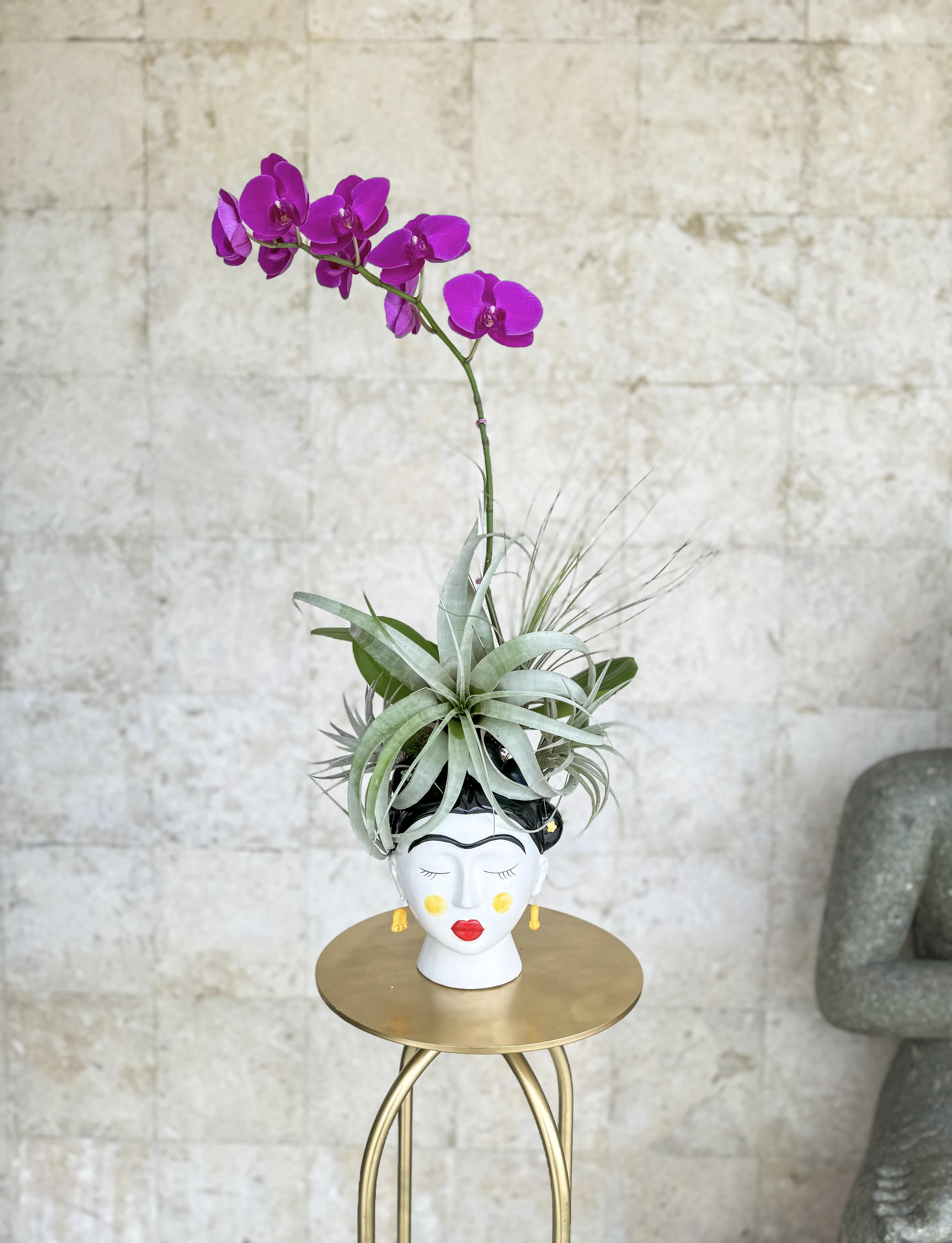 Purple orchid in a decorative face-shaped planter with air plants
