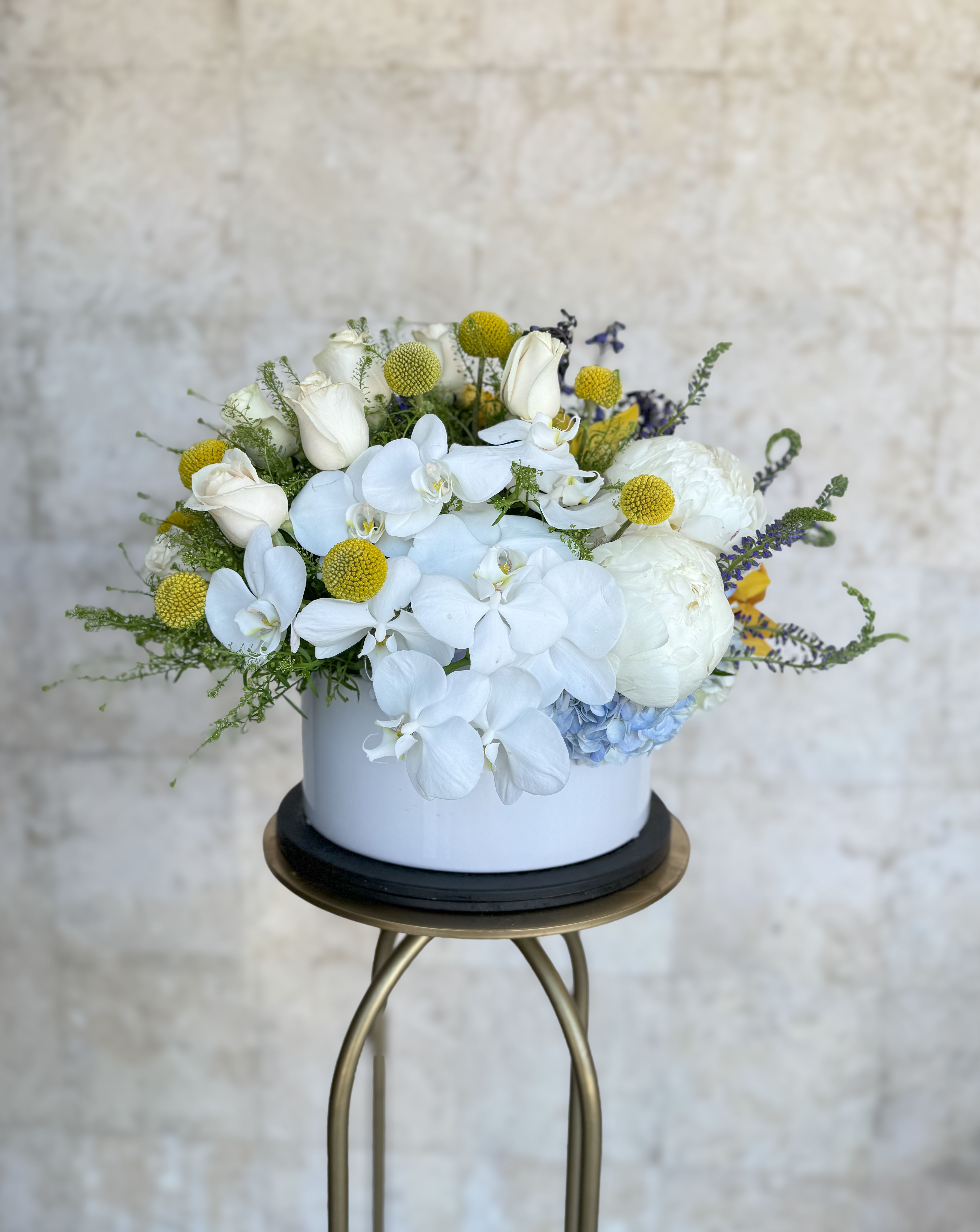 White orchids and roses in a round white vase with yellow accents
