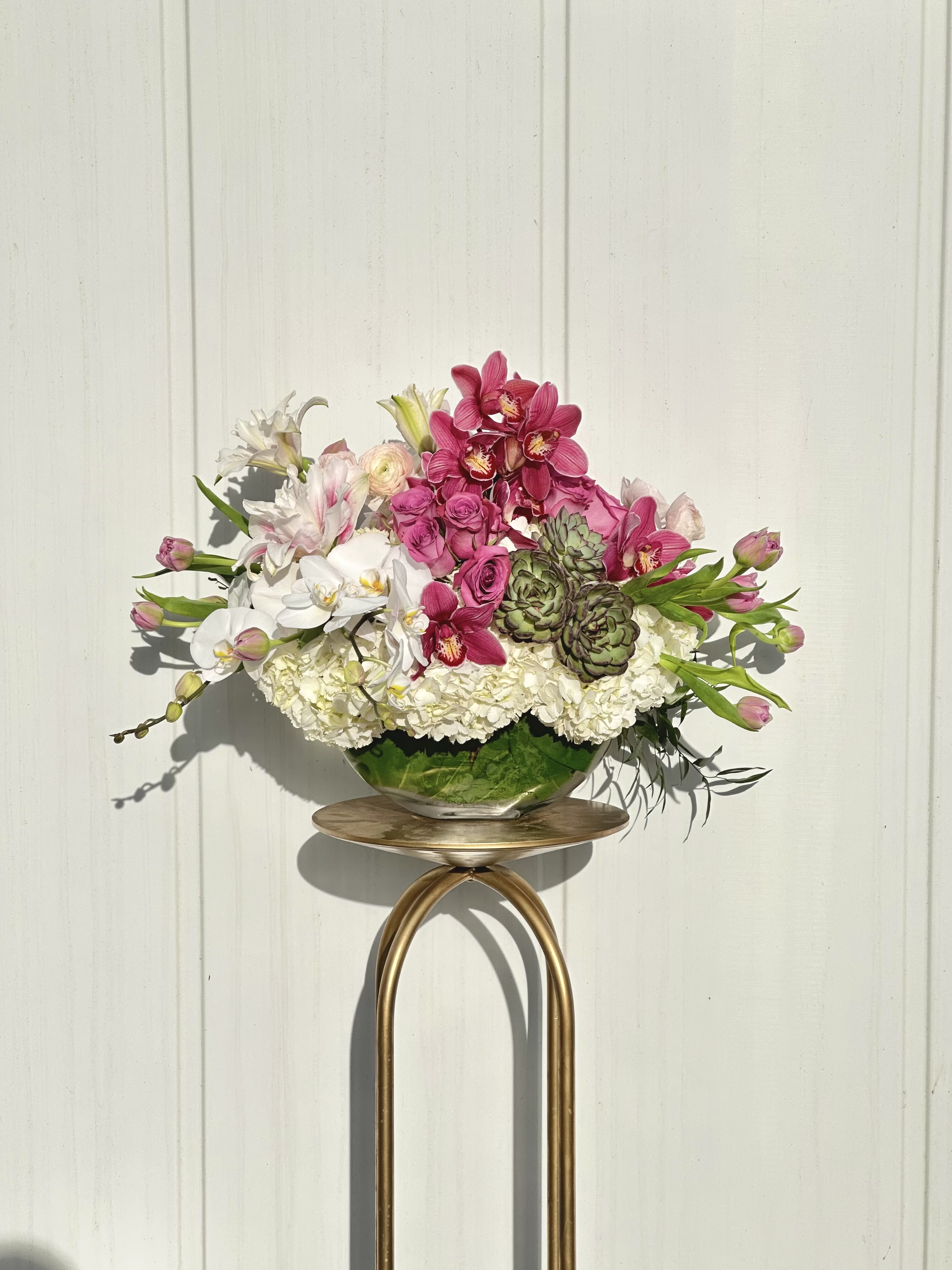 Pink and white floral arrangement in a glass bowl on a gold stand