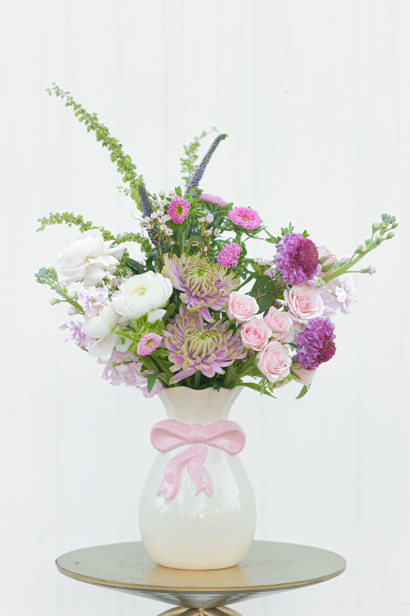 Pink and white mixed flower arrangement in a white vase with a pink bow