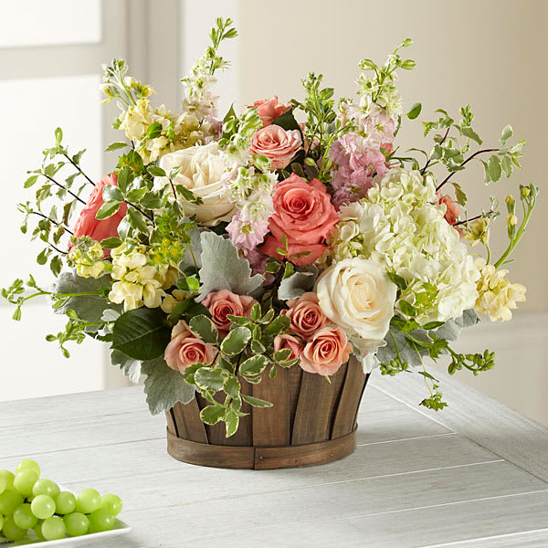 Mixed bouquet of pink and white roses with pale blooms in a wooden basket