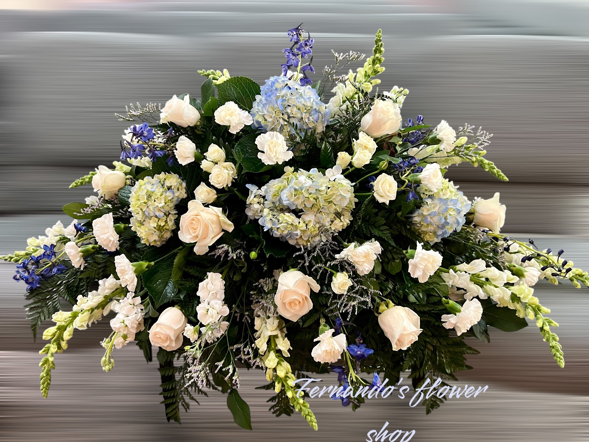 Large white and blue casket spray with roses, hydrangeas, and carnations in an elongated design