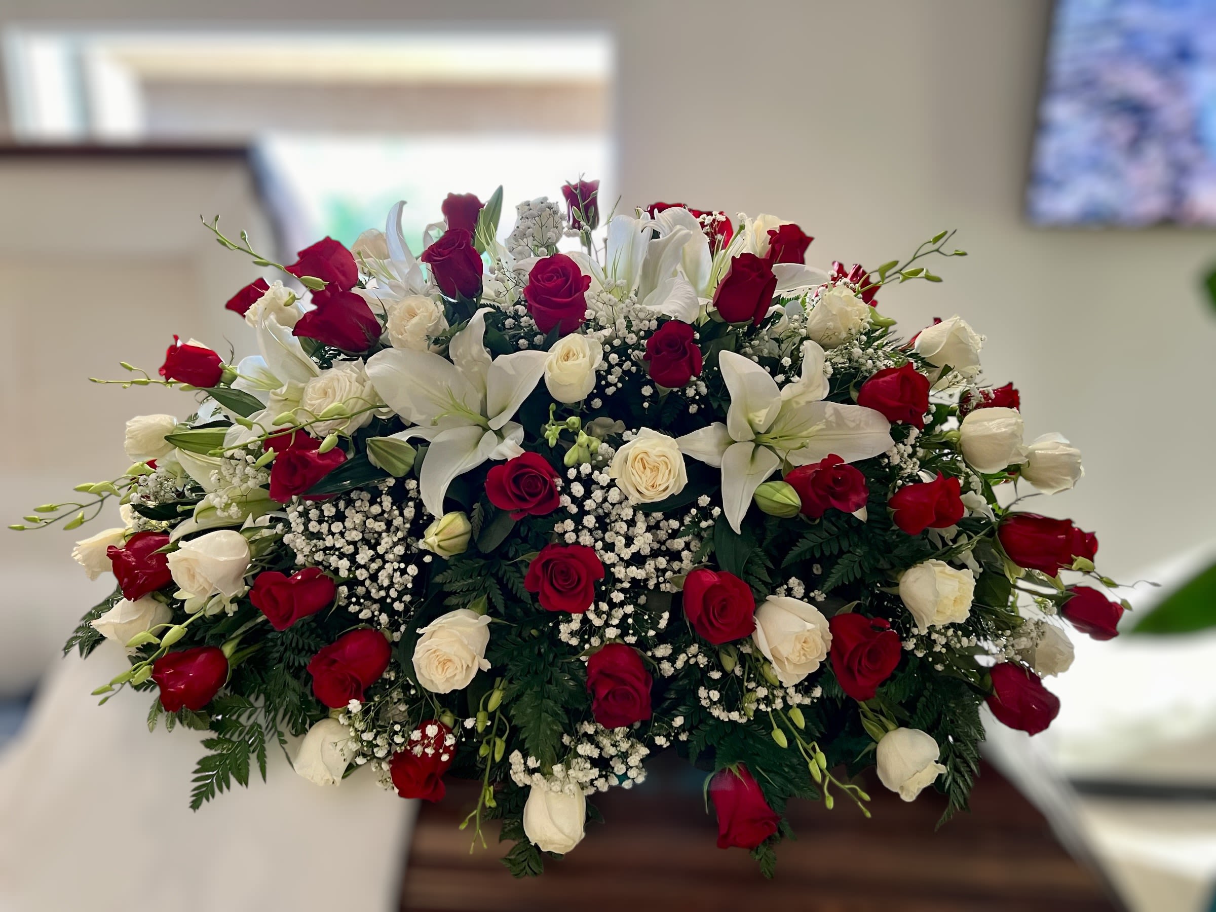 Large red and white rose and lily spray arranged on top of a casket