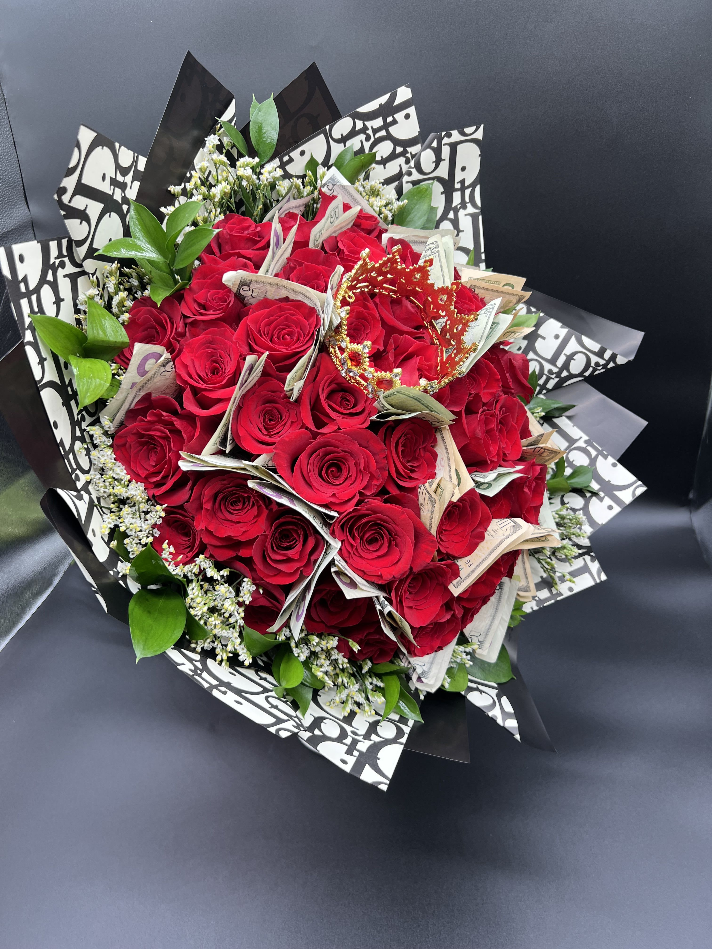 Bouquet of red roses accented with folded currency and a small red crown in patterned wrap