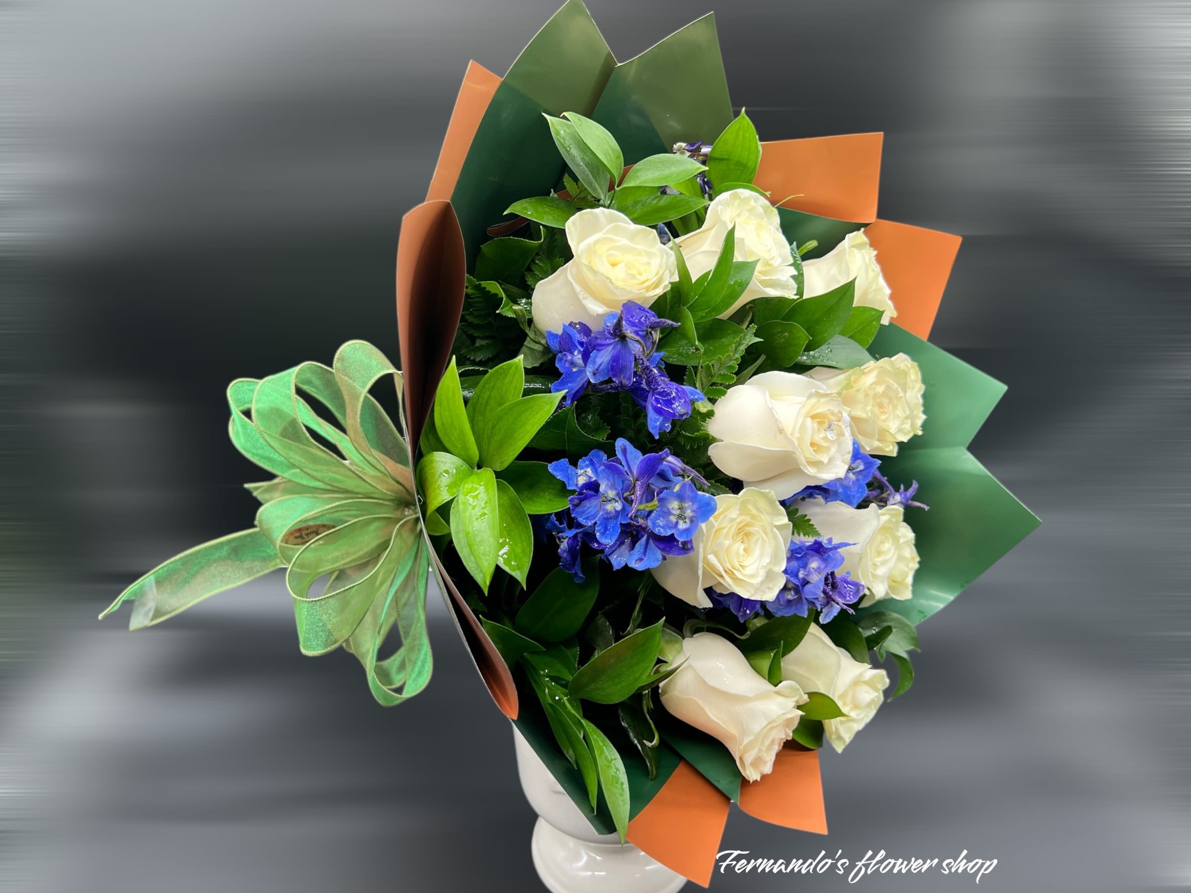 Bouquet of white roses and blue delphinium in colorful wrap with a green bow