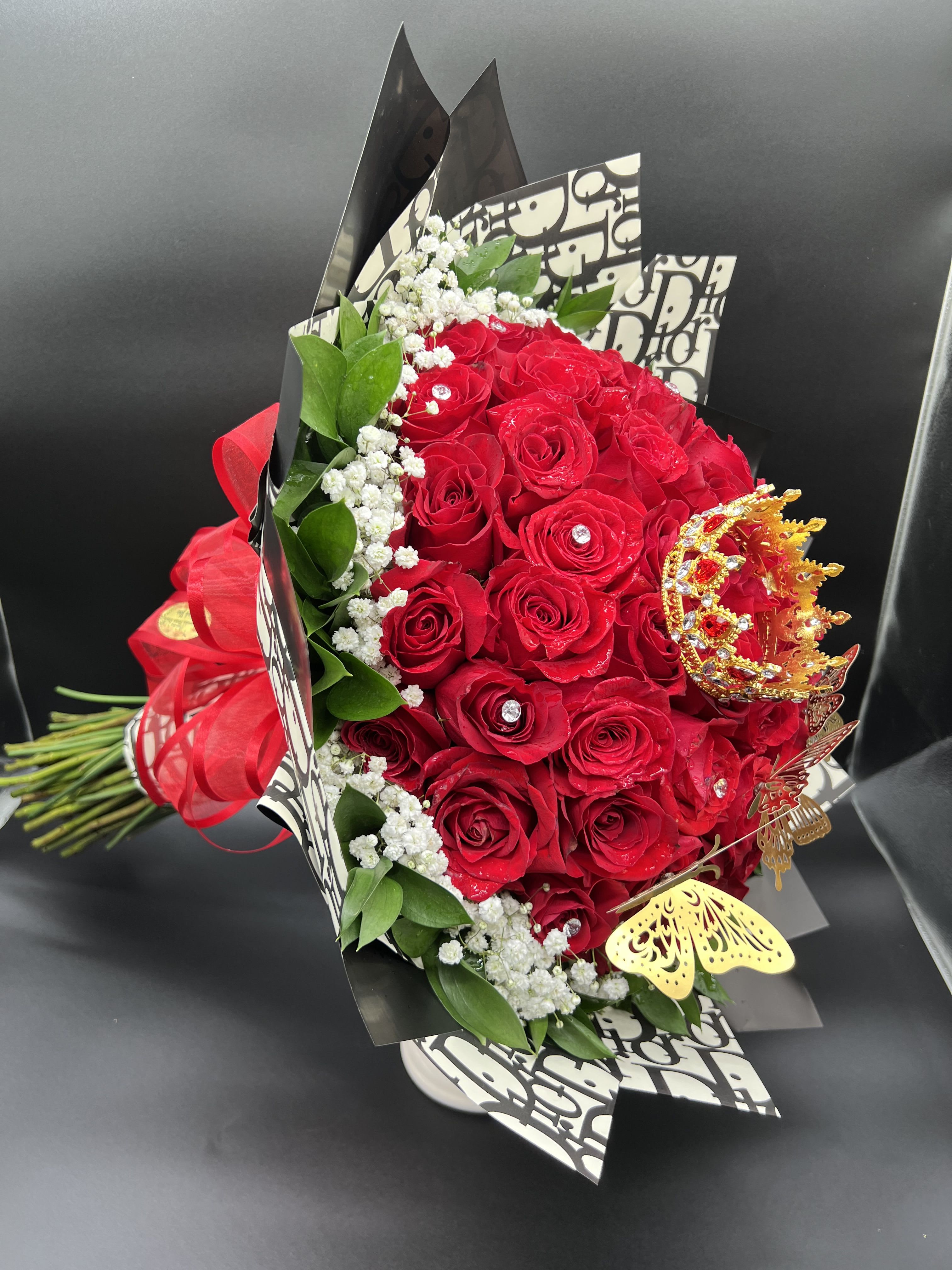 Hand-tied bouquet of red roses with baby's breath, jeweled accents, and gold crown decor.