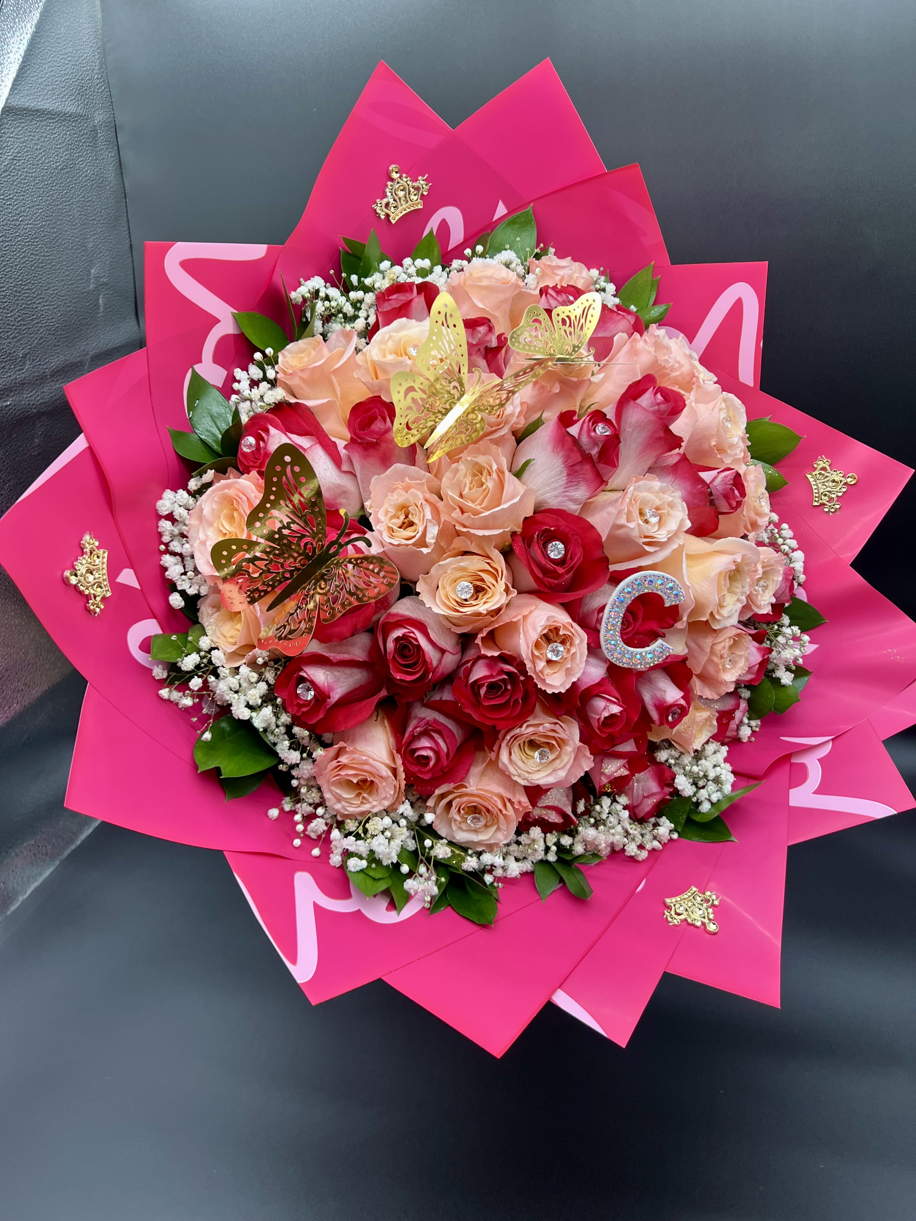 Round bouquet of red and peach roses wrapped in bright pink paper with gold butterfly accents.
