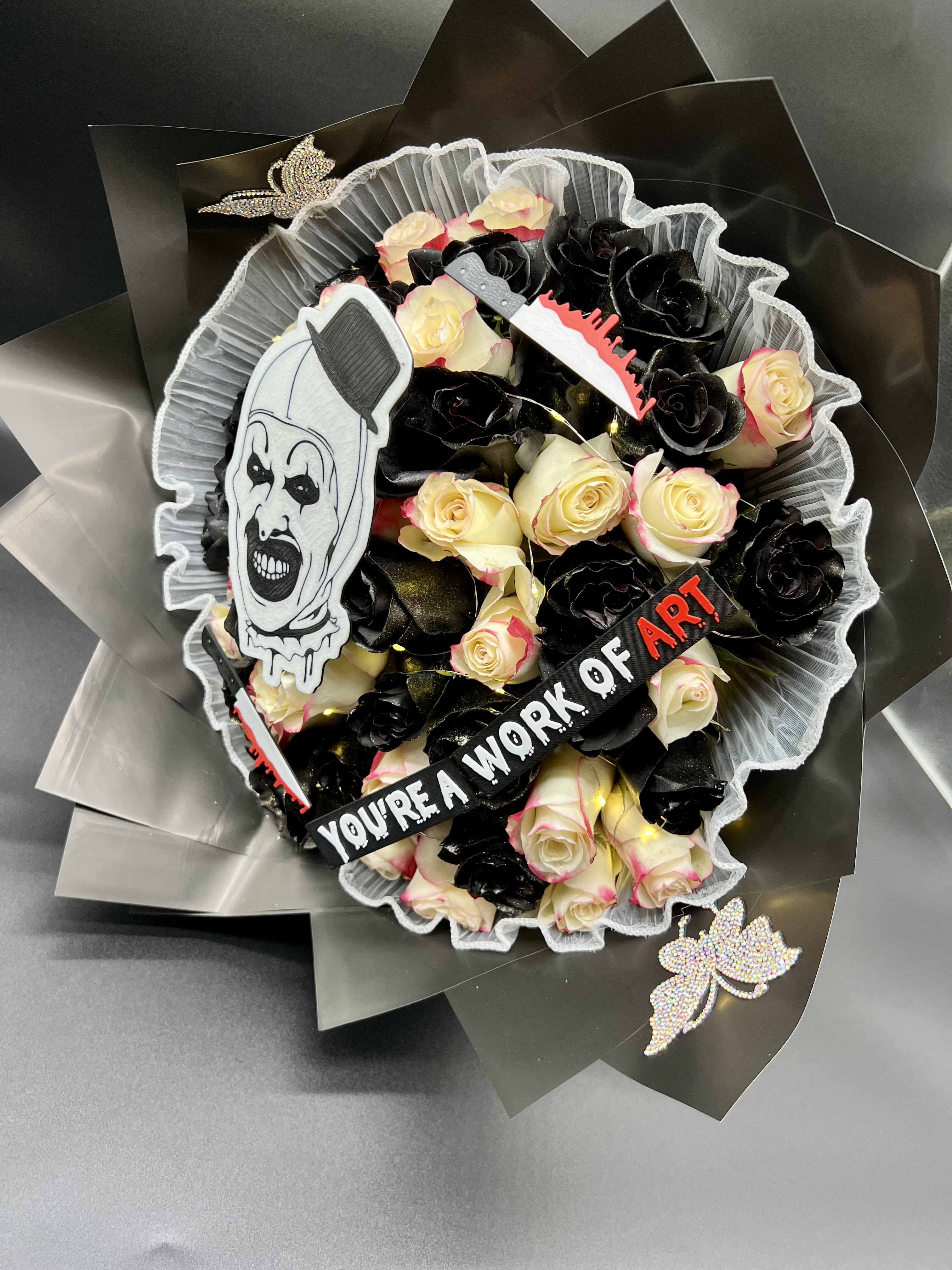 Bouquet of cream and black roses with horror clown decoration and a ribbon reading you’re a work of art.