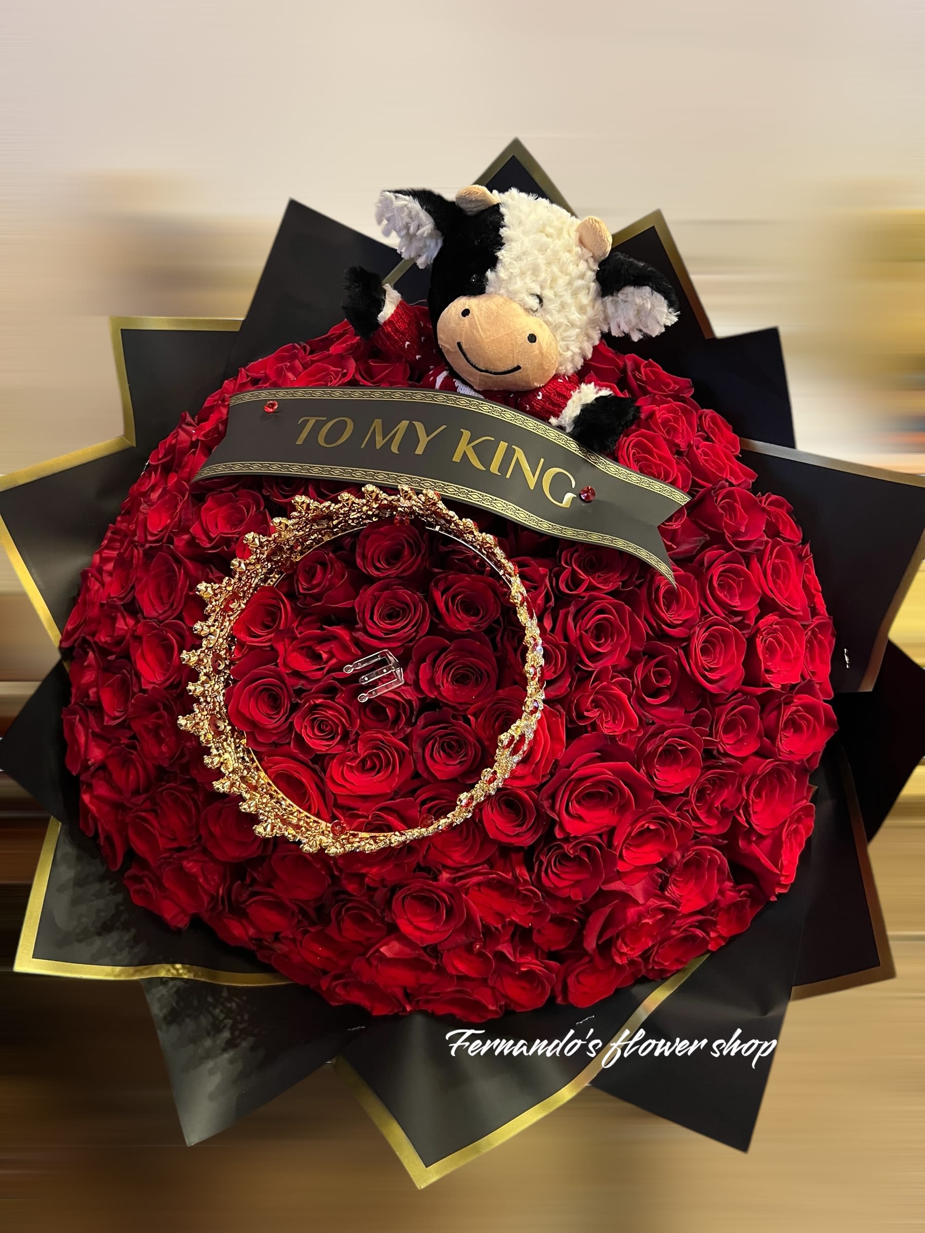 Large round bouquet of red roses with a plush cow, gold crown, and 'To My King' ribbon on black and gold wrap.