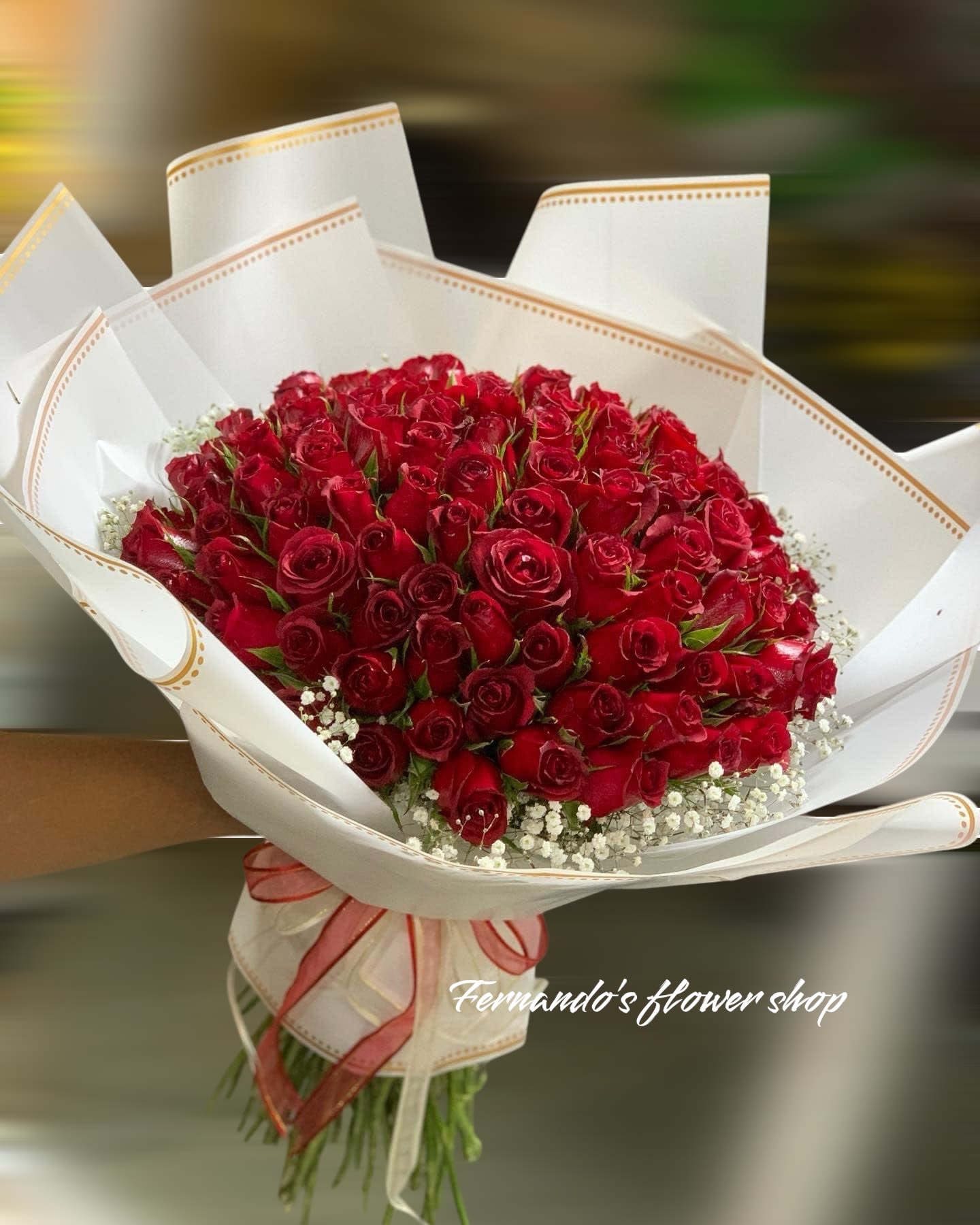 Large bouquet of red roses with white filler flowers wrapped in white paper and tied with a ribbon