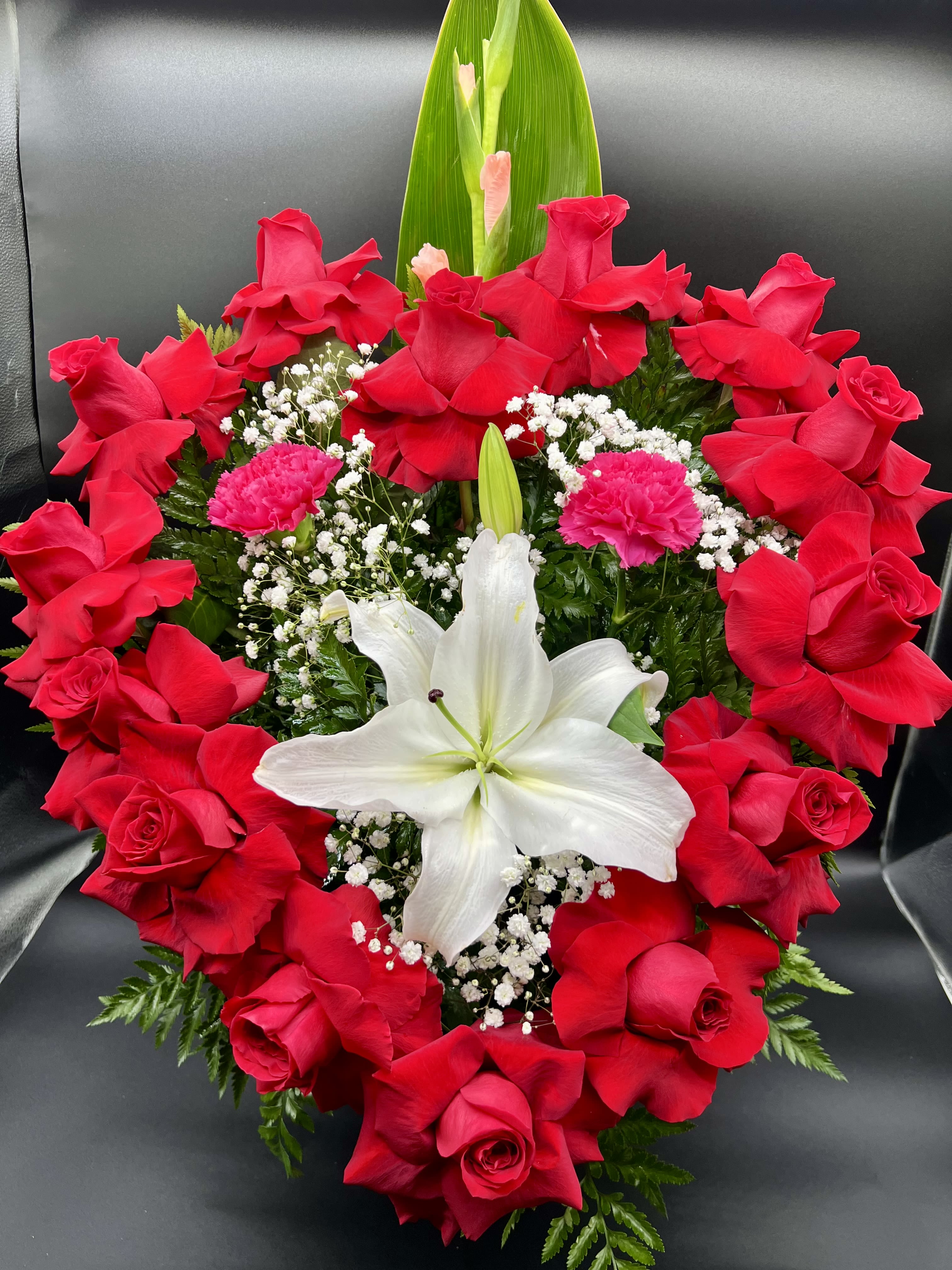 Heart-shaped arrangement of red roses with a central white lily and pink carnations