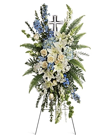 Tall white and blue standing spray with lilies and roses on an easel with a silver cross