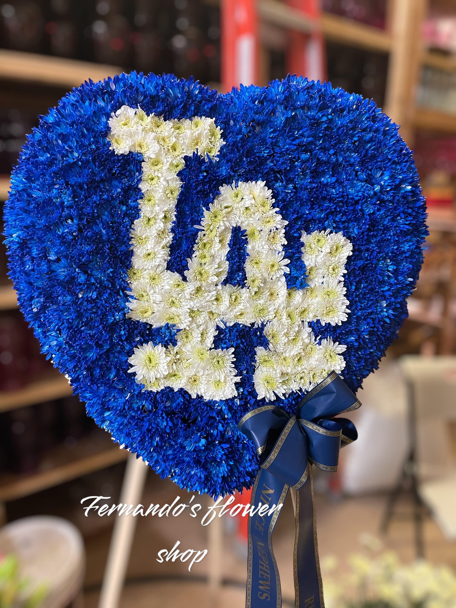 Heart-shaped blue and white floral standing spray with a monogram design and blue ribbon bow.