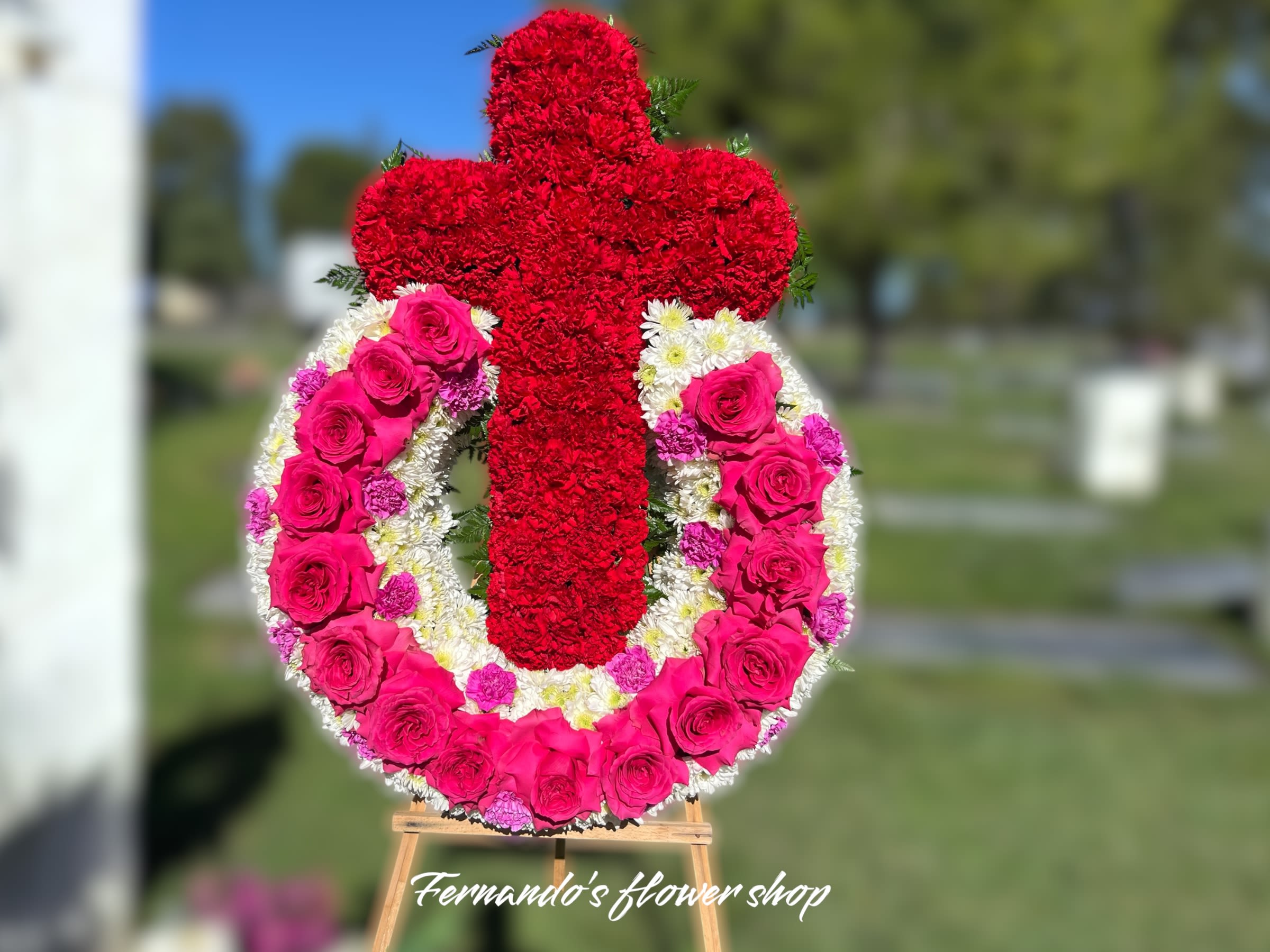 Standing funeral wreath of pink roses and white mums with a red carnation cross on an easel