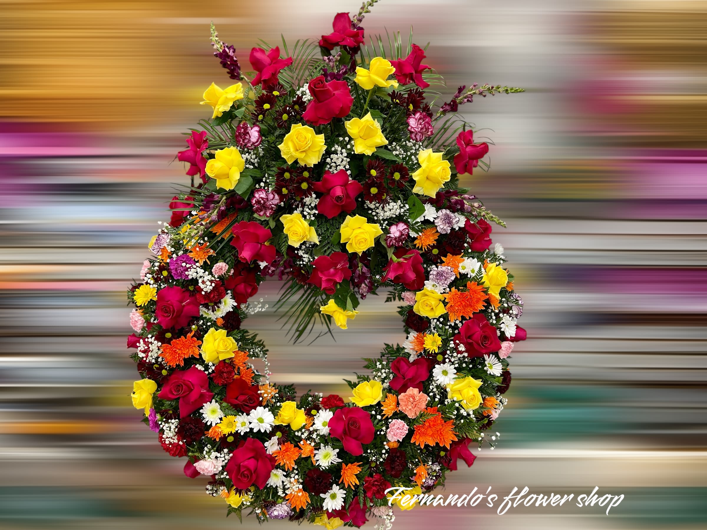 Circular wreath of red and yellow roses with mixed orange and white flowers in a dense design
