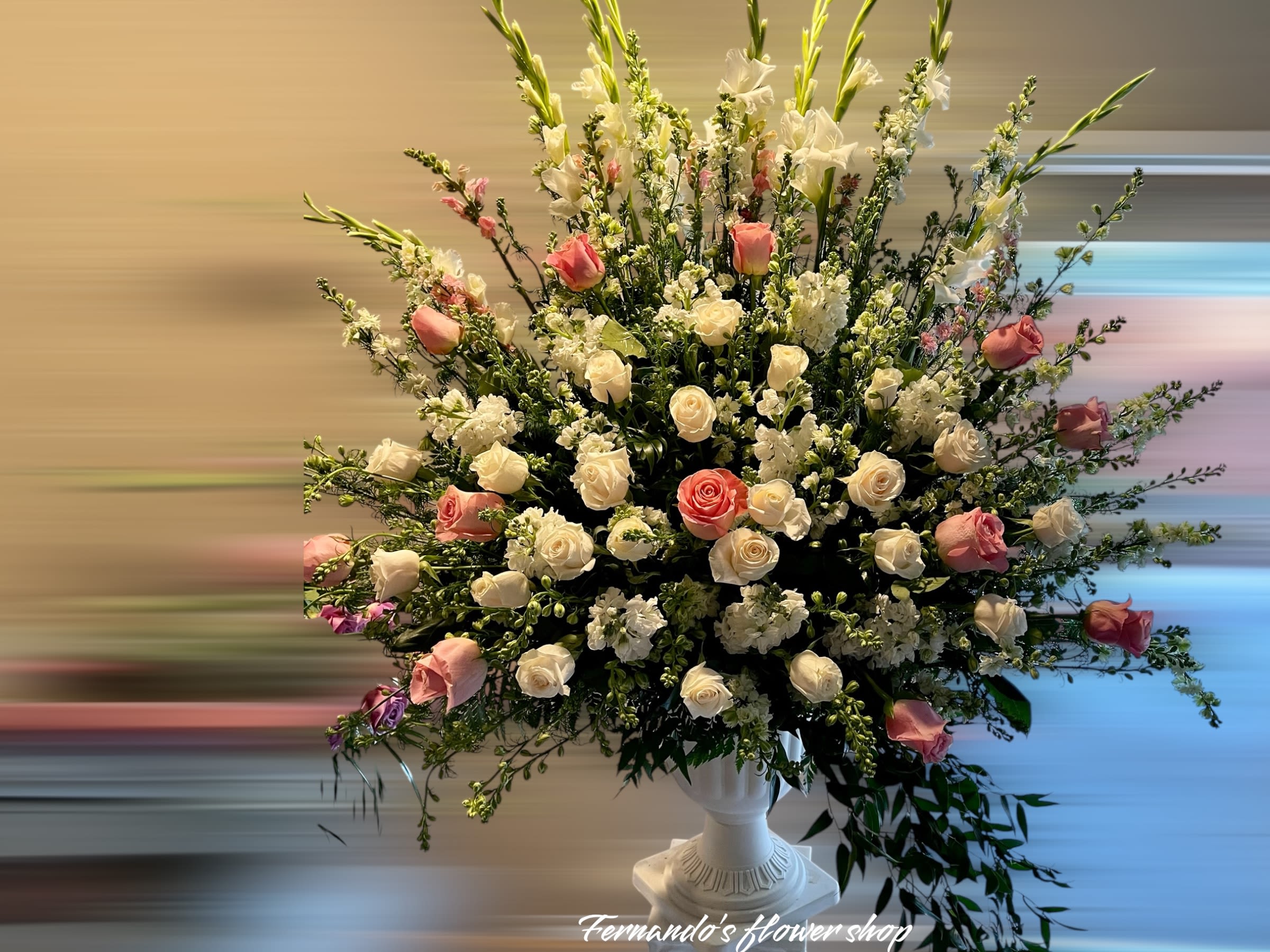 Large fan-shaped arrangement of white and pink roses with tall white blooms in a white pedestal vase