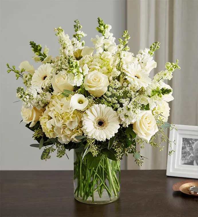 Large all-white flower arrangement with roses and gerberas in a clear glass vase