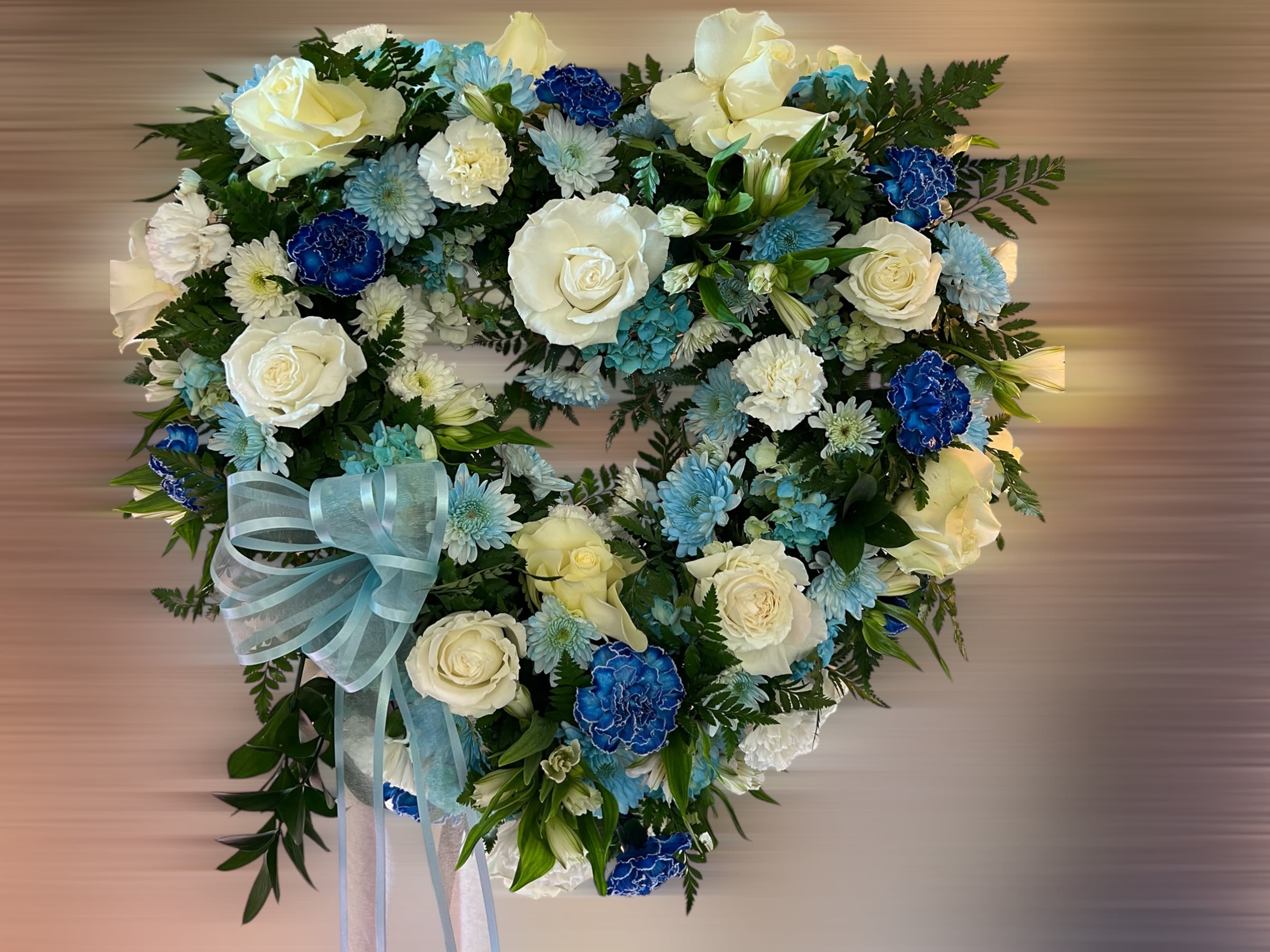 Heart-shaped wreath of white roses and blue carnations with a light blue ribbon bow
