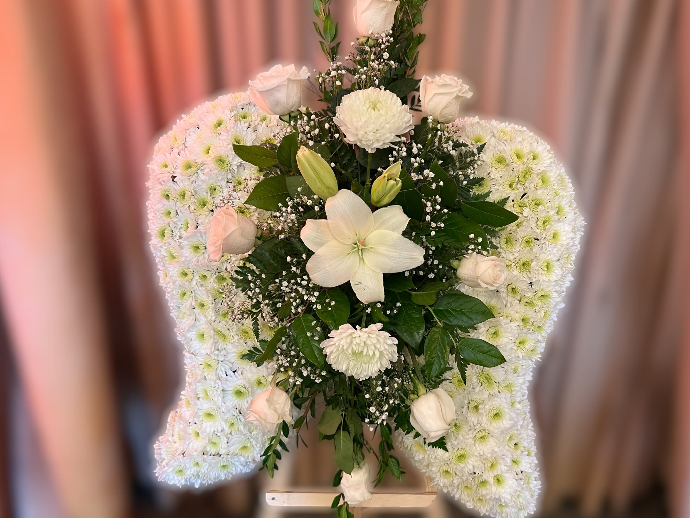 Standing white floral arrangement with chrysanthemum wings and central roses and lilies