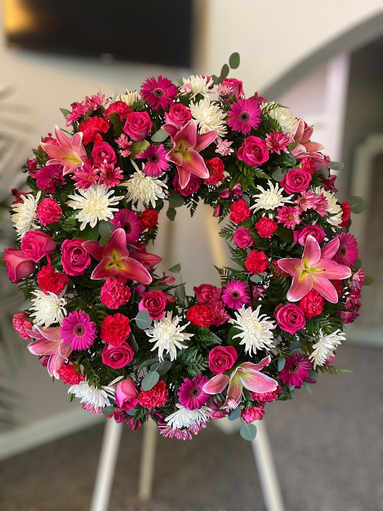 Standing wreath of pink lilies, roses, gerbera daisies and white chrysanthemums on an easel