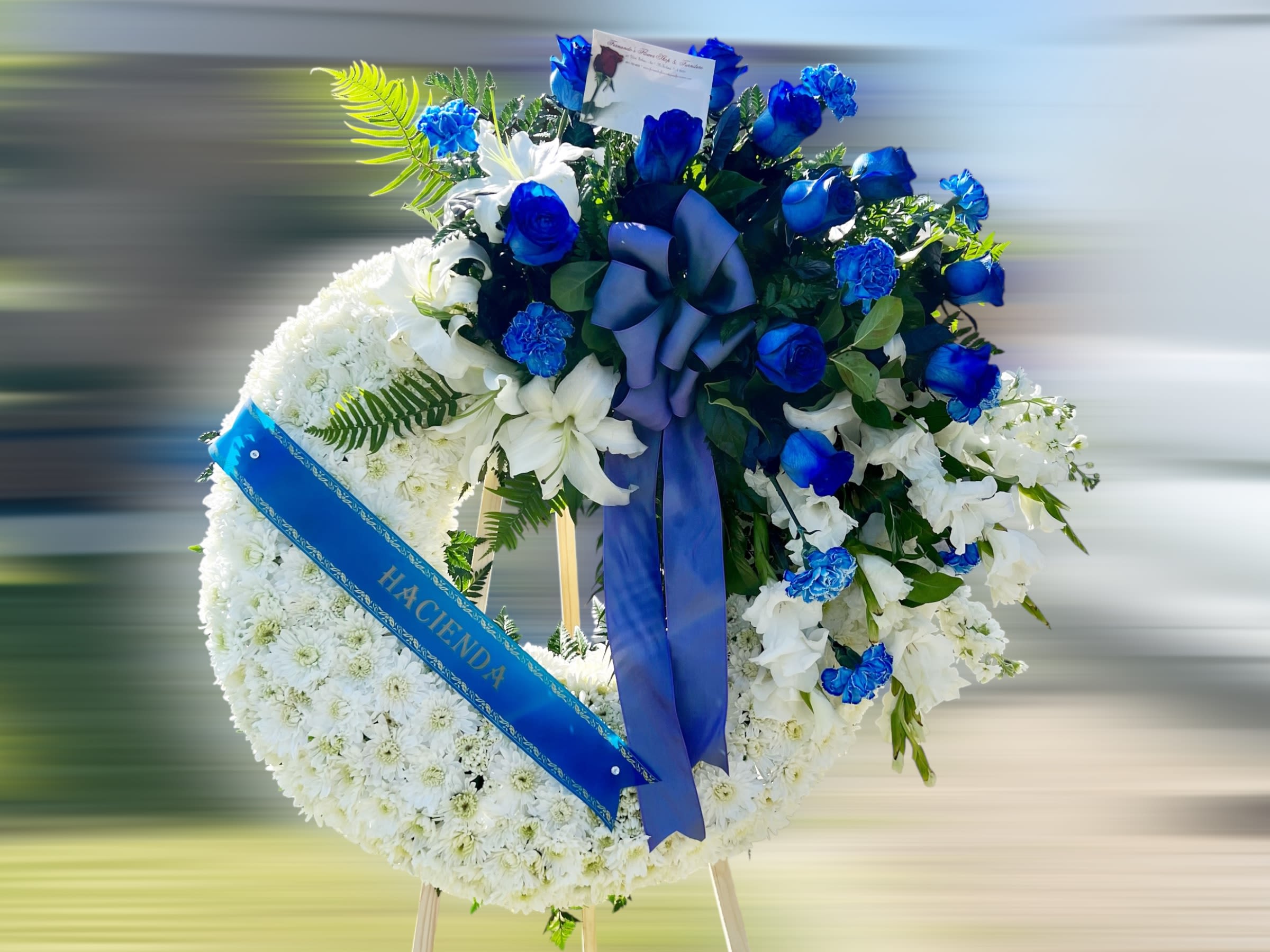 Standing white sympathy wreath with blue roses and ribbon on an easel