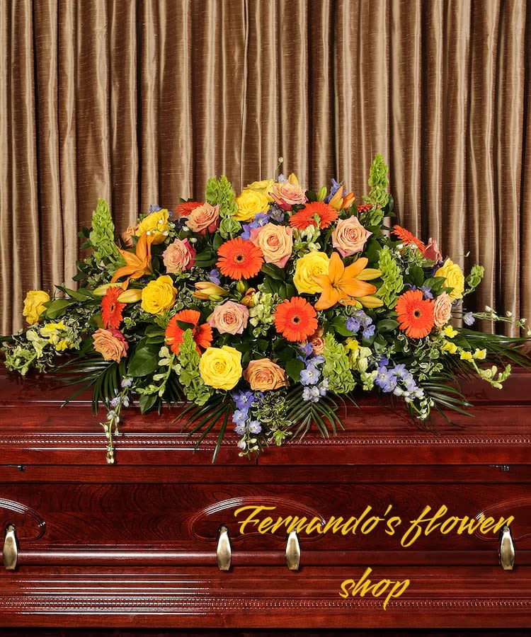 Bright orange and yellow casket spray with roses, gerbera daisies, and lilies on a wooden casket