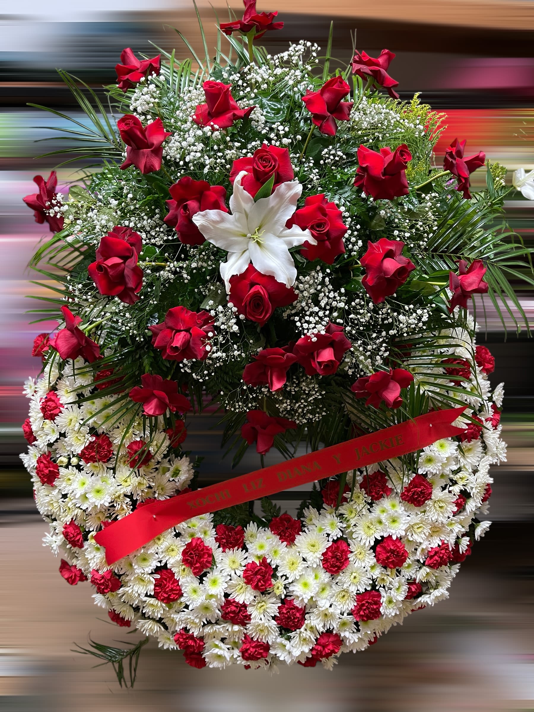 Large red and white funeral wreath with roses, lilies, and carnations on a standing frame