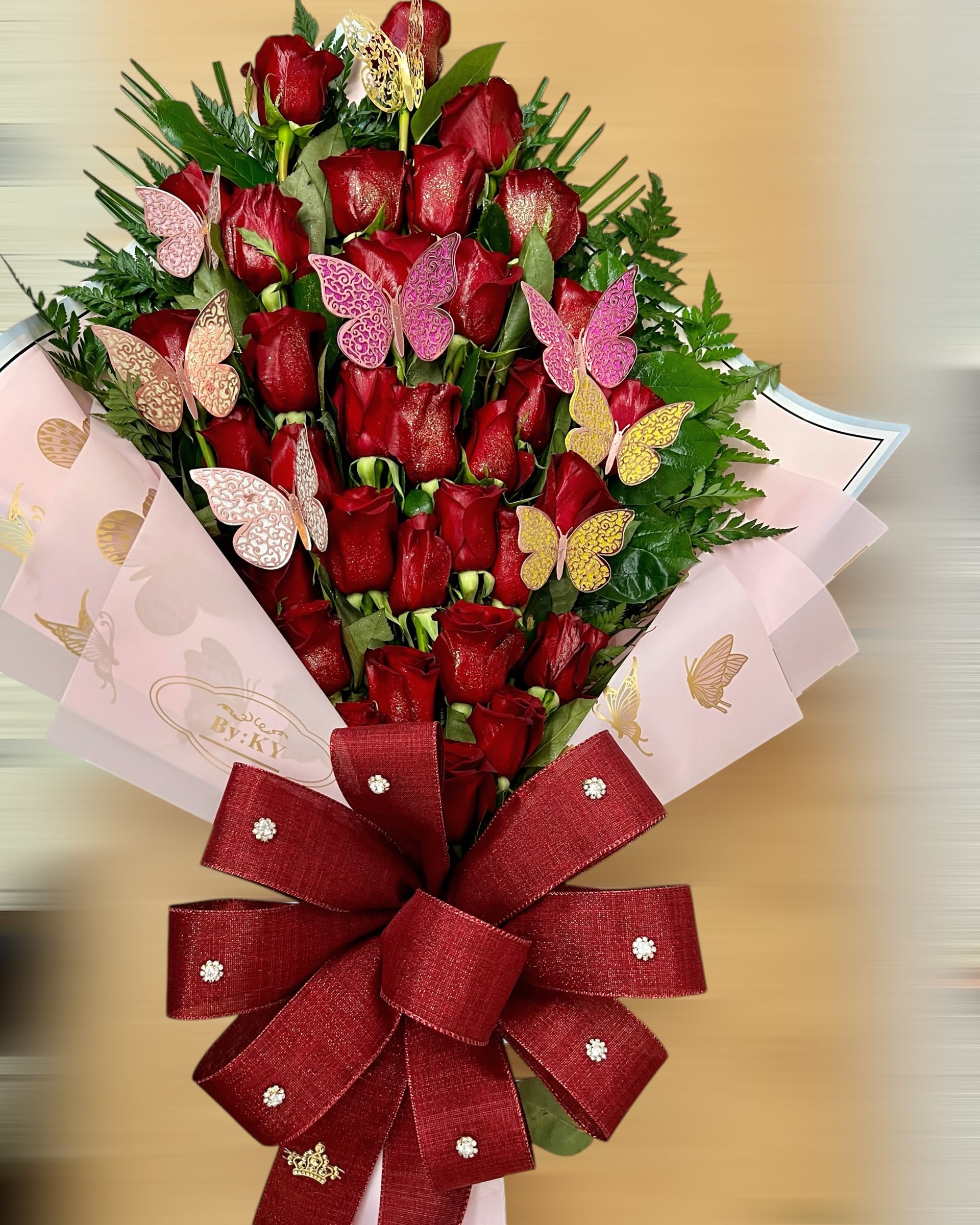 Tall bouquet of red roses with pink butterflies and a large red bow in pink wrap