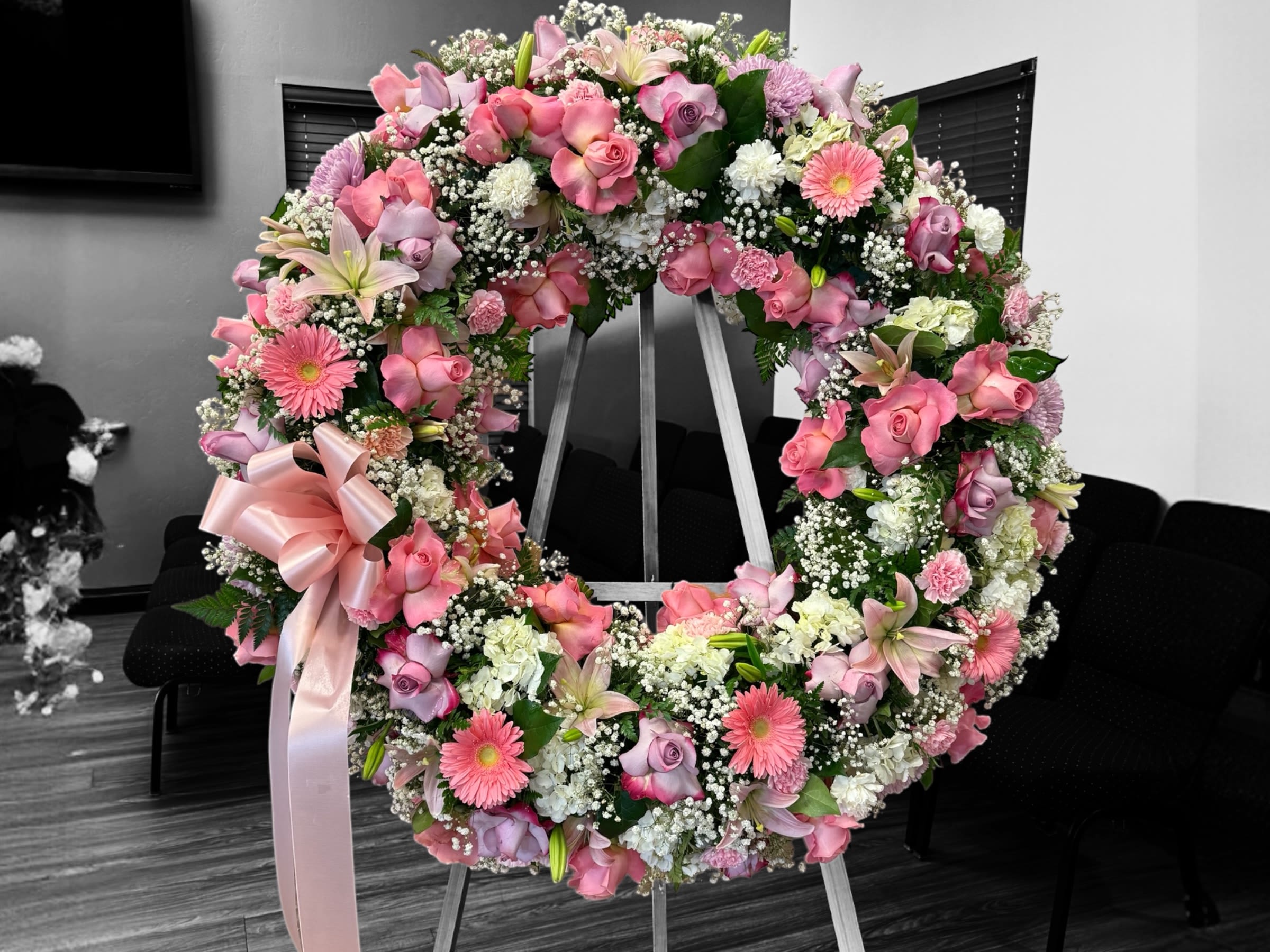 Large pink and white floral wreath with roses, lilies, and gerberas on an easel