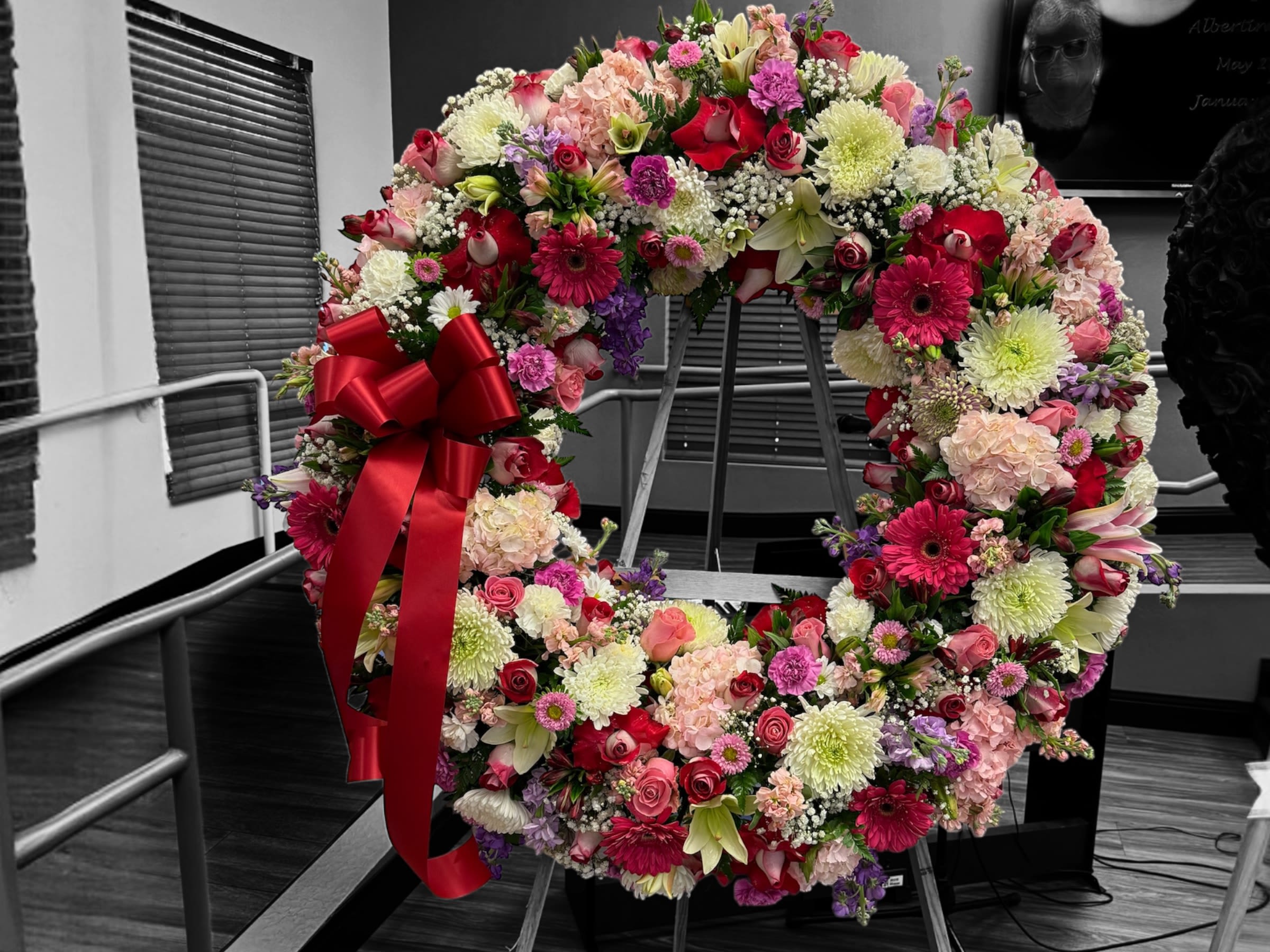 Large standing wreath of pink, red, and white flowers with a red bow on an easel