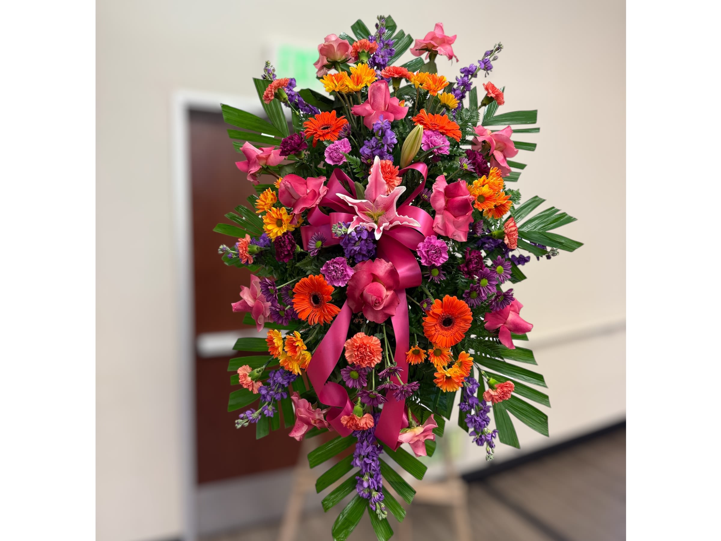 Tall standing spray of bright pink, orange, and purple flowers with a large pink bow