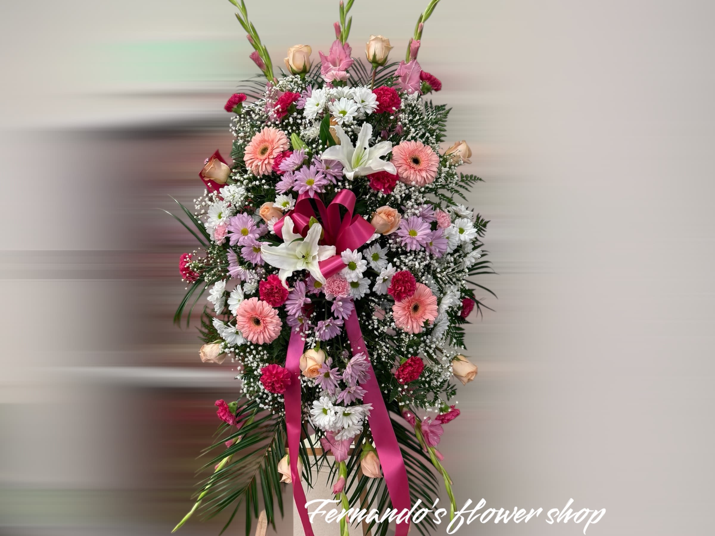 Tall standing spray of pink, white, and peach flowers with a pink ribbon on an easel
