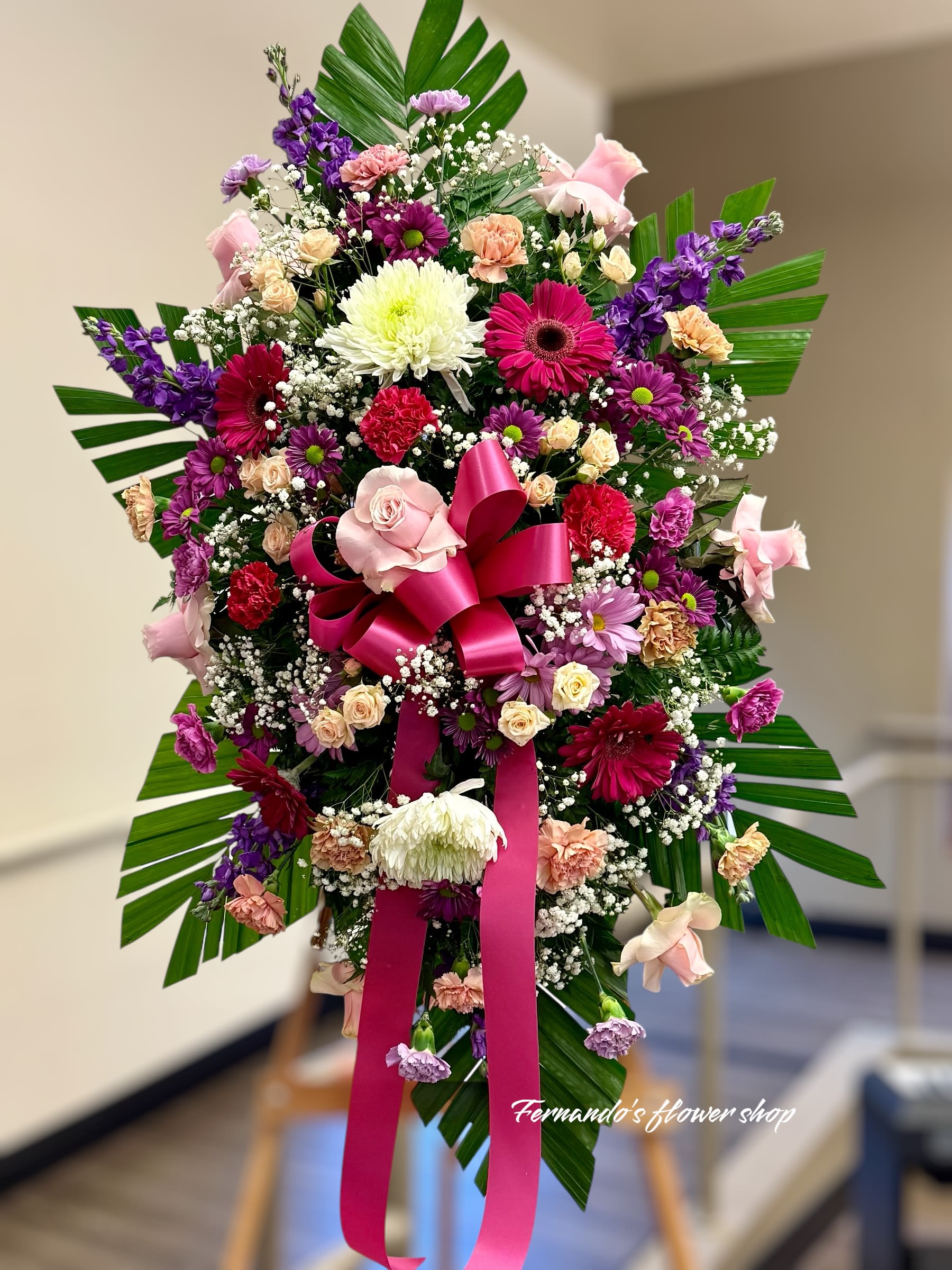 Tall standing spray of pink, purple, and white flowers with a large hot pink bow on an easel