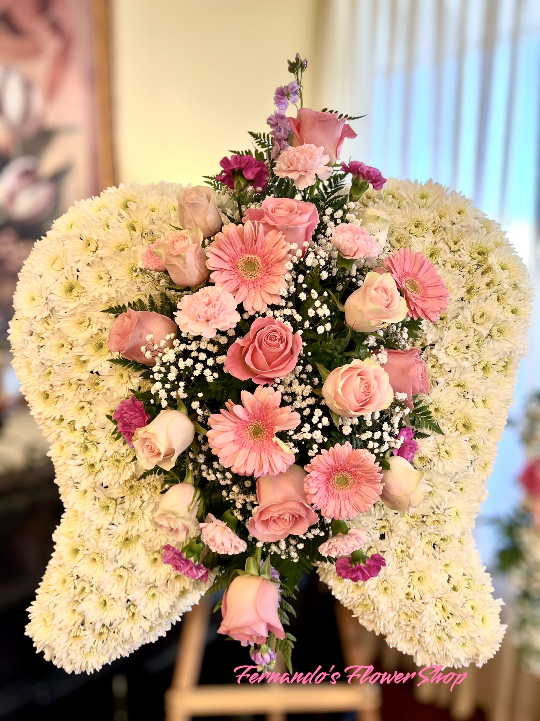Angel wing-shaped white mum spray with pink roses and gerbera daisies on an easel