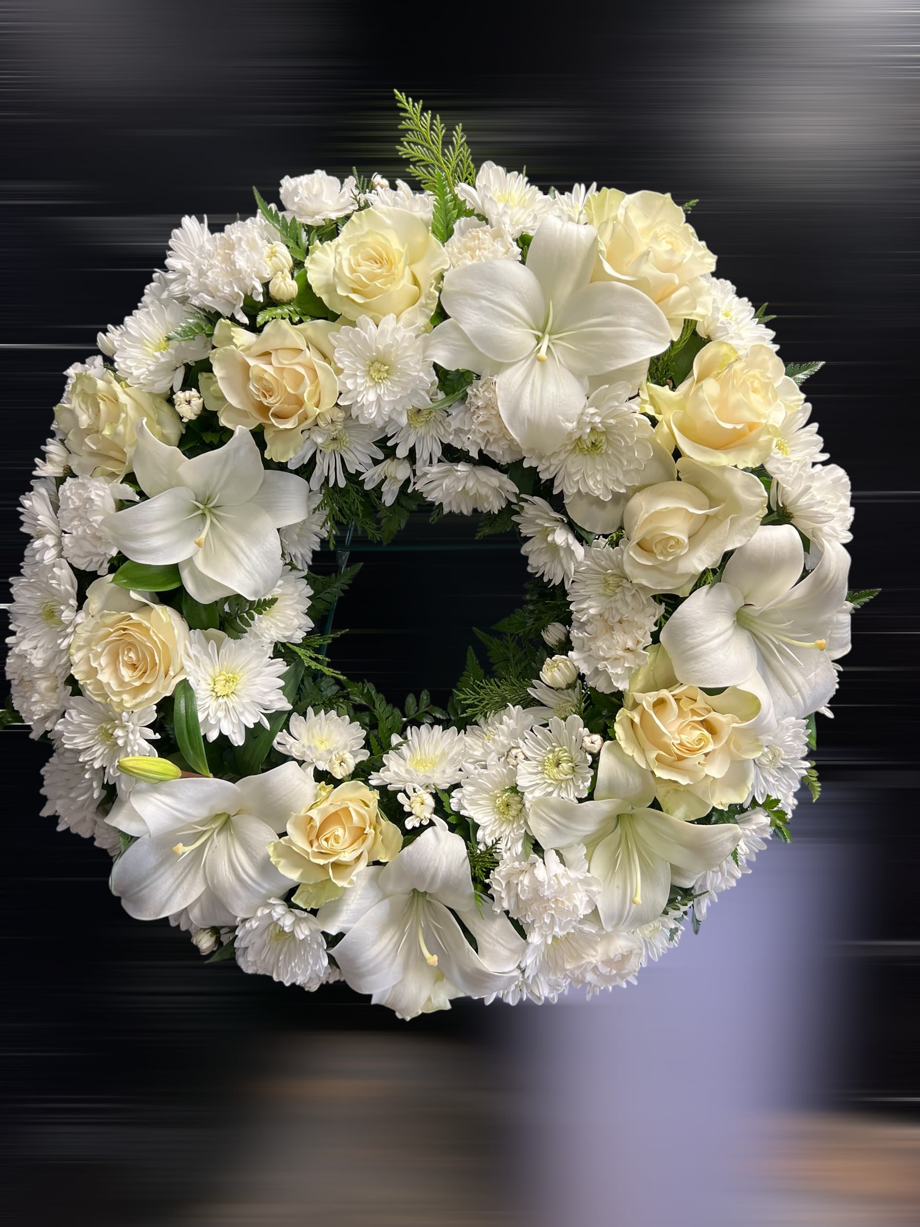 Round wreath of white lilies, cream roses, and white chrysanthemums on a dark background