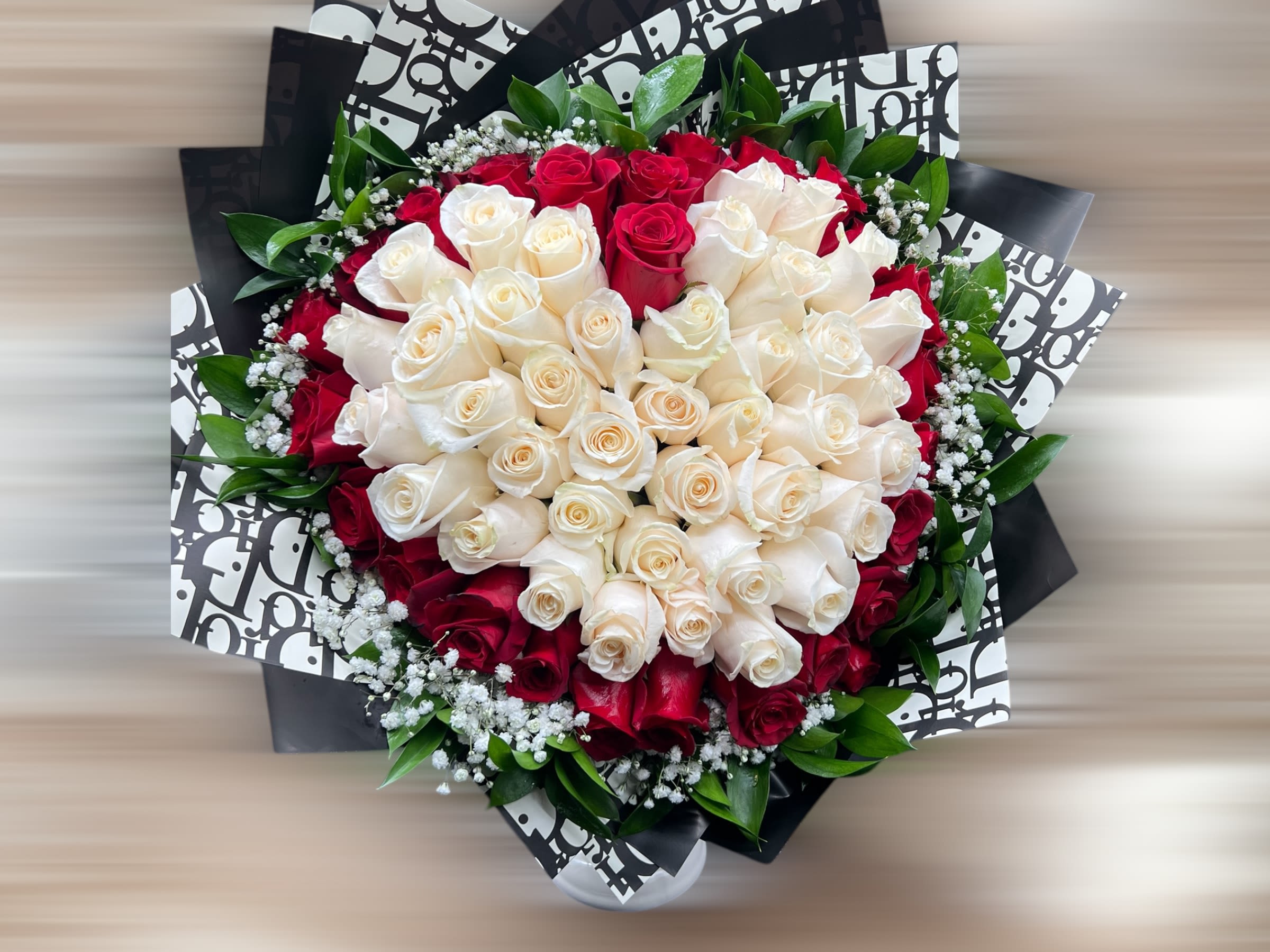 Round bouquet of cream and red roses with baby's breath, wrapped in black and white patterned paper.