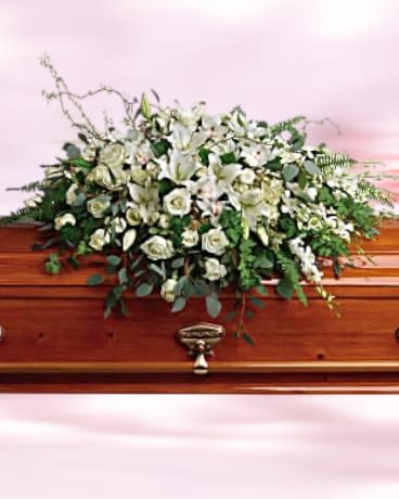 White lilies and roses arranged as a casket spray on a polished wood coffin