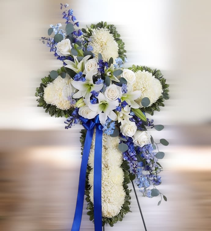 Standing cross of white mums with white lilies and roses, blue delphinium, and blue ribbon