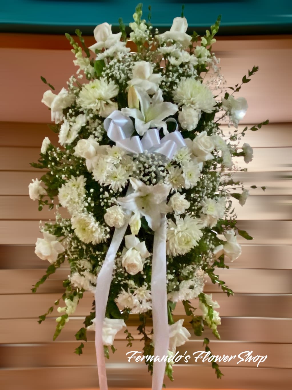 Tall white sympathy standing spray with roses, lilies, and mums accented by a white ribbon bow
